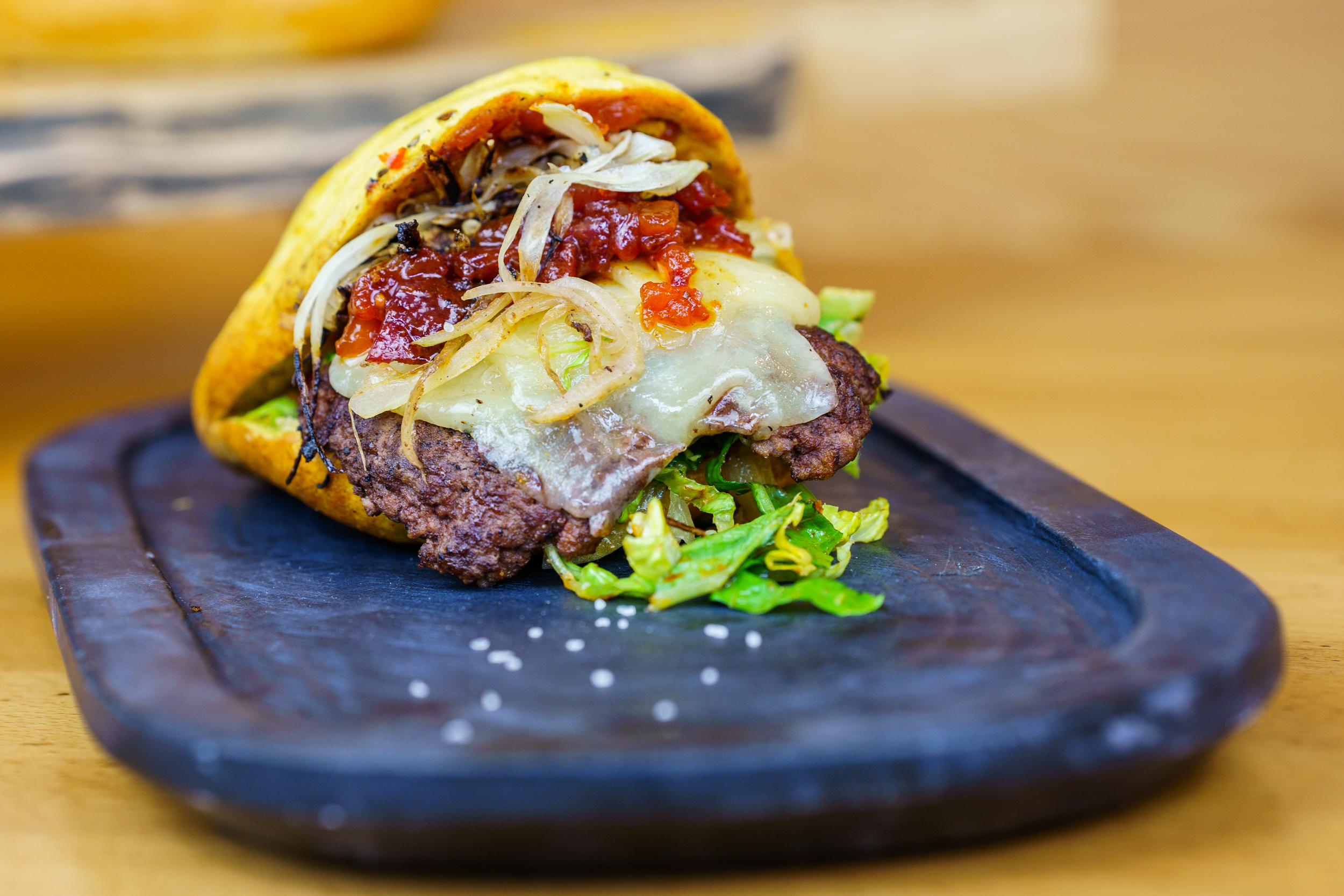 An open-faced burger with saucy toppings laid out on a black slate serving platter.