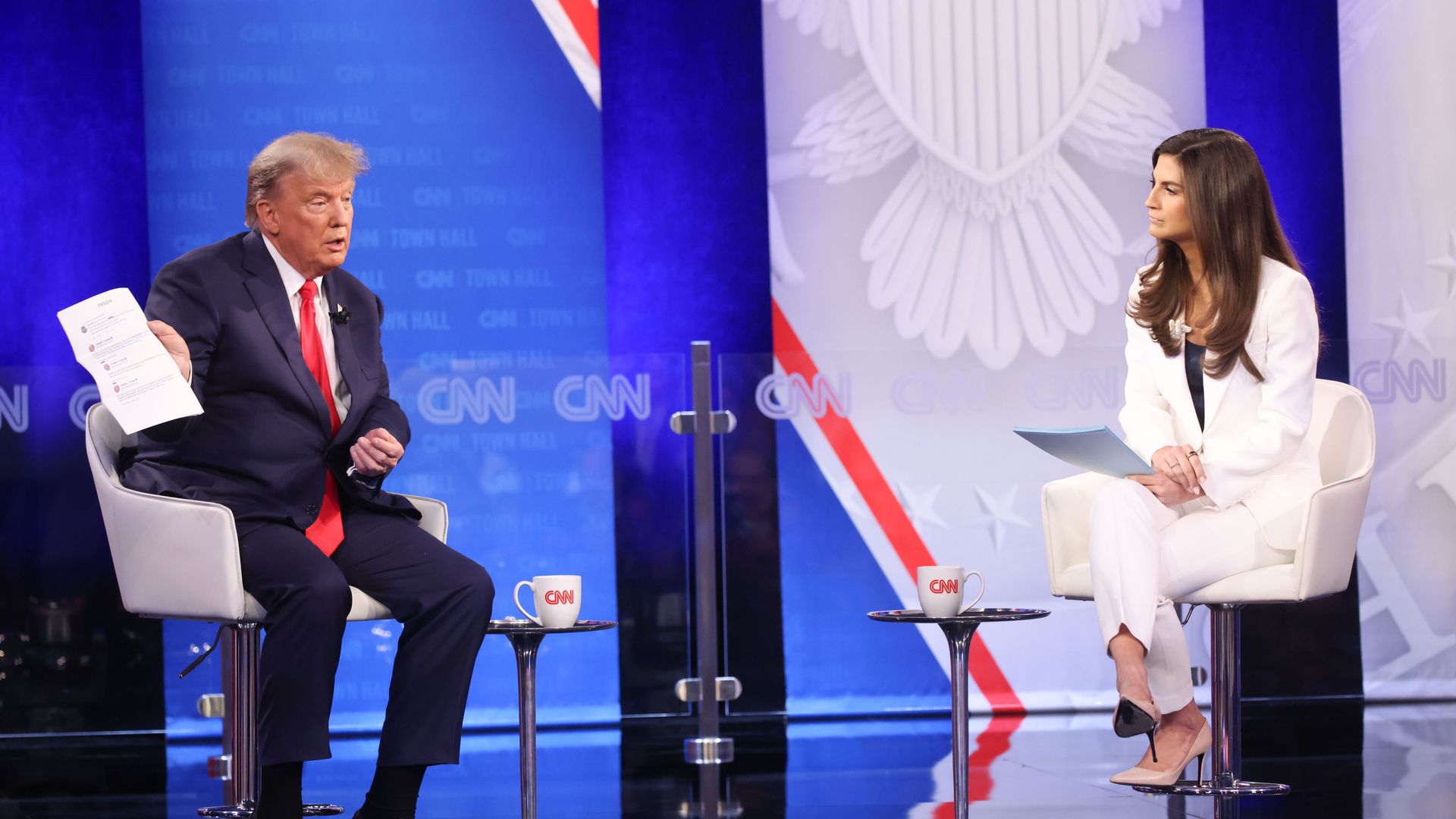 Former President Donald Trump sitting onstage, showing the interviewer a piece of paper.