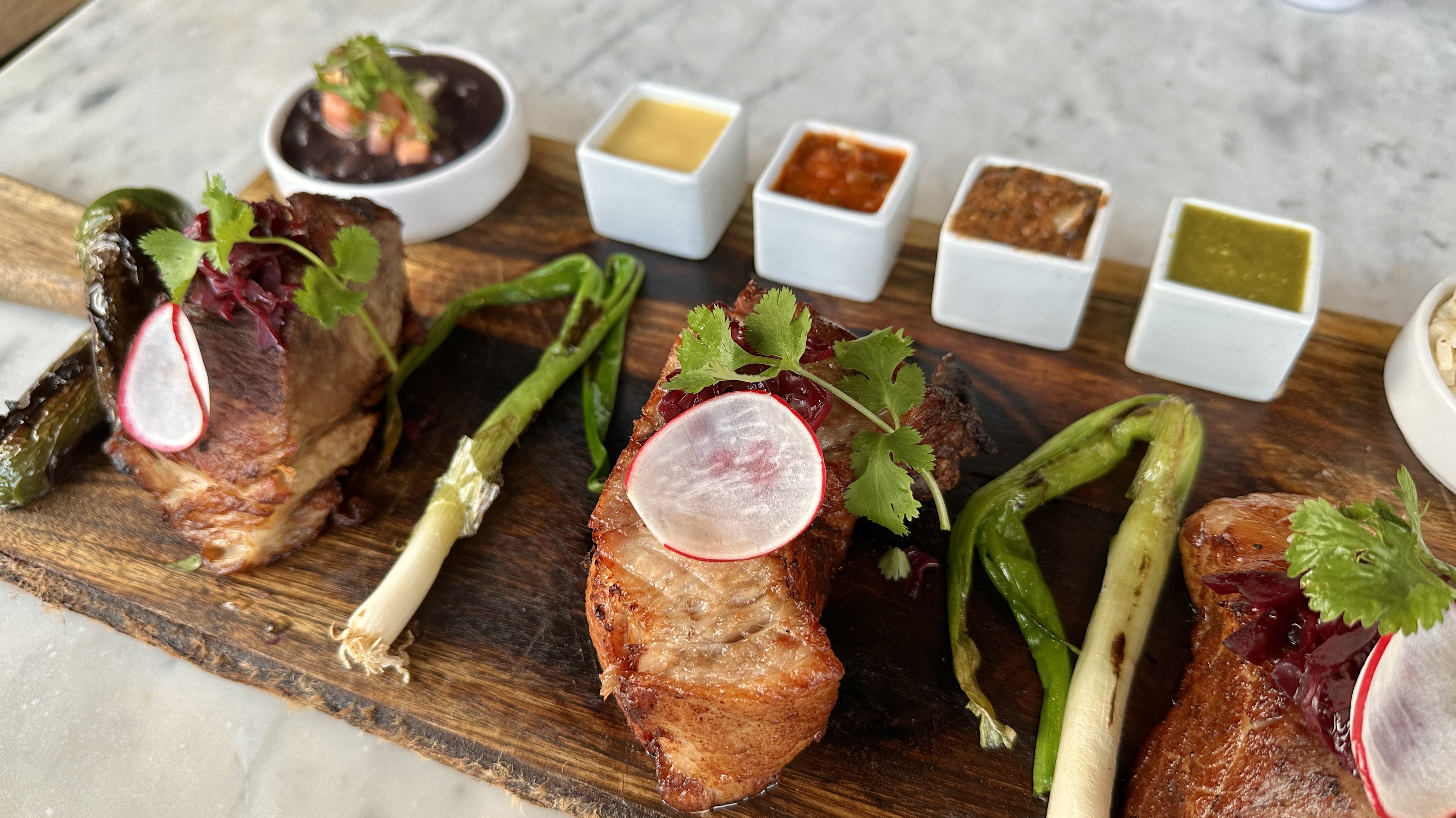 A selection of meats served on a wooden board with sauces and sides.