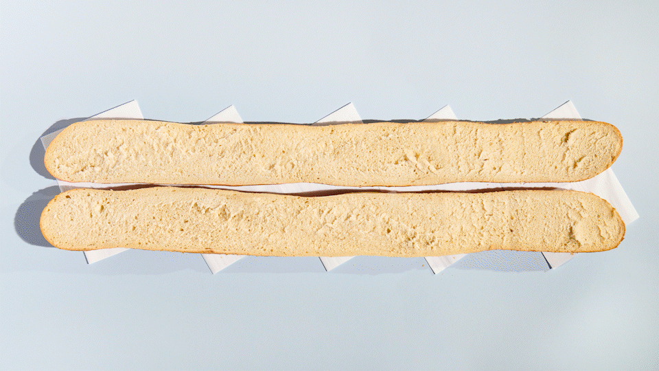 A giant hoagie with relish, meats, cheeses, and greens is assembled and cut into pieces. GIF.