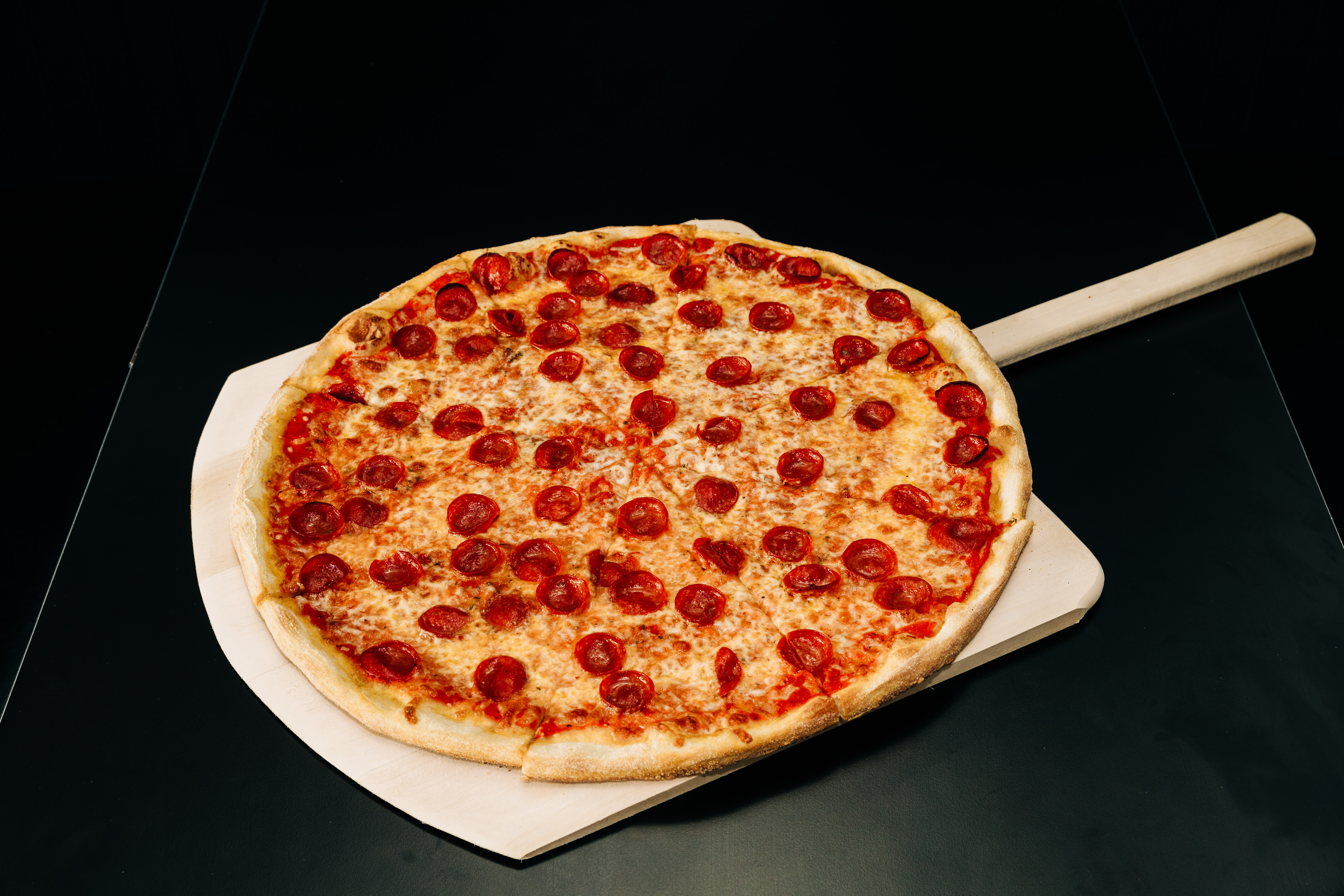 A pepperoni pizza on a wooden pizza peel is visible against a black background.