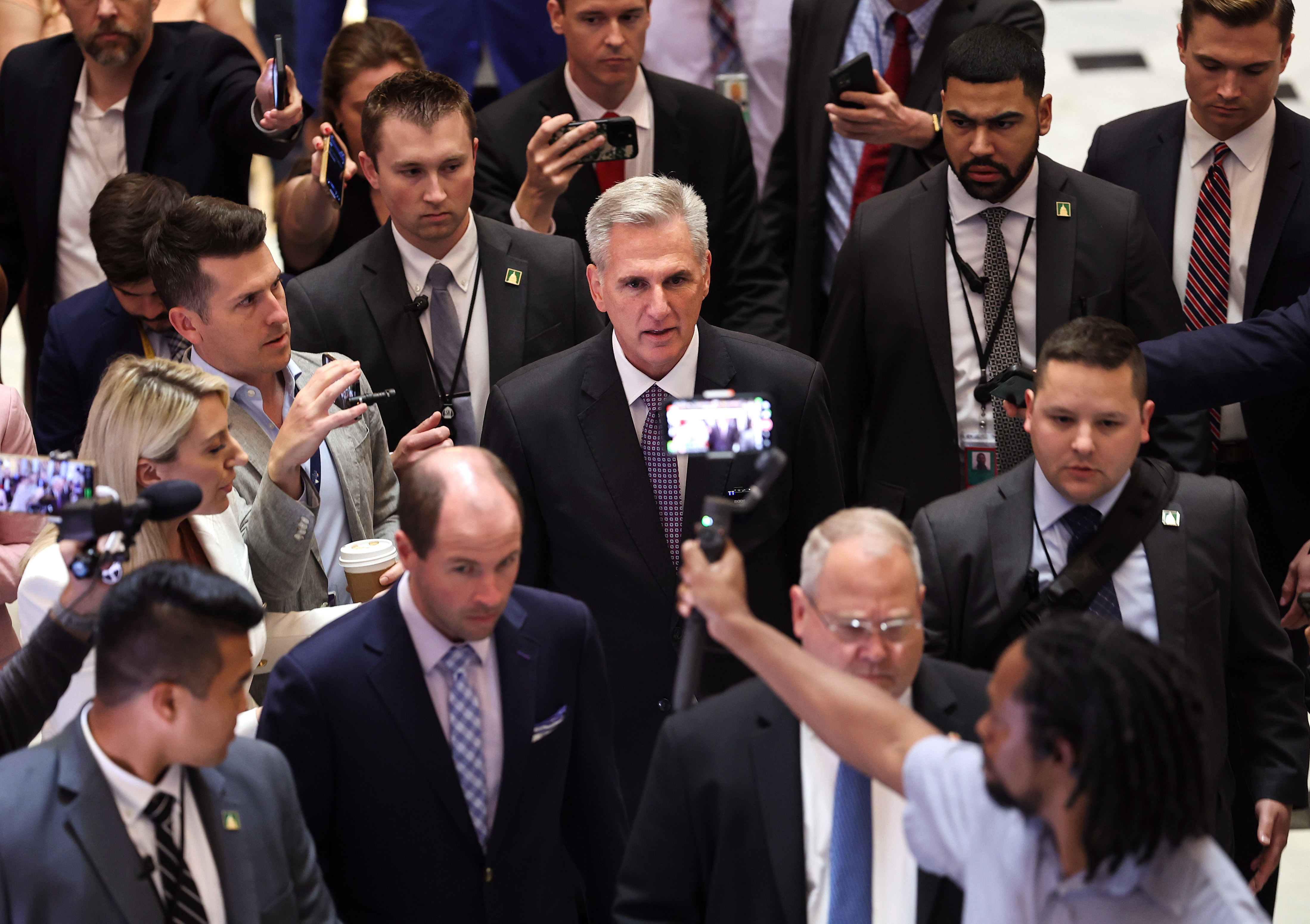 A crowd of people in suits and ties surround Kevin McCarthy, pointing microphones at him and taking videos with their cellphones.