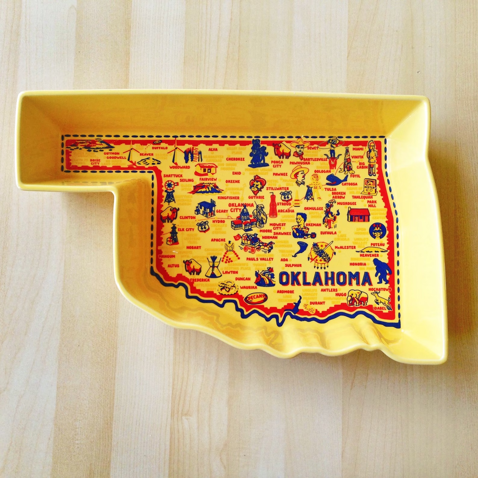 A yellow casserole dish shaped like Oklahoma with small illustrations of state landmarks on the bottom