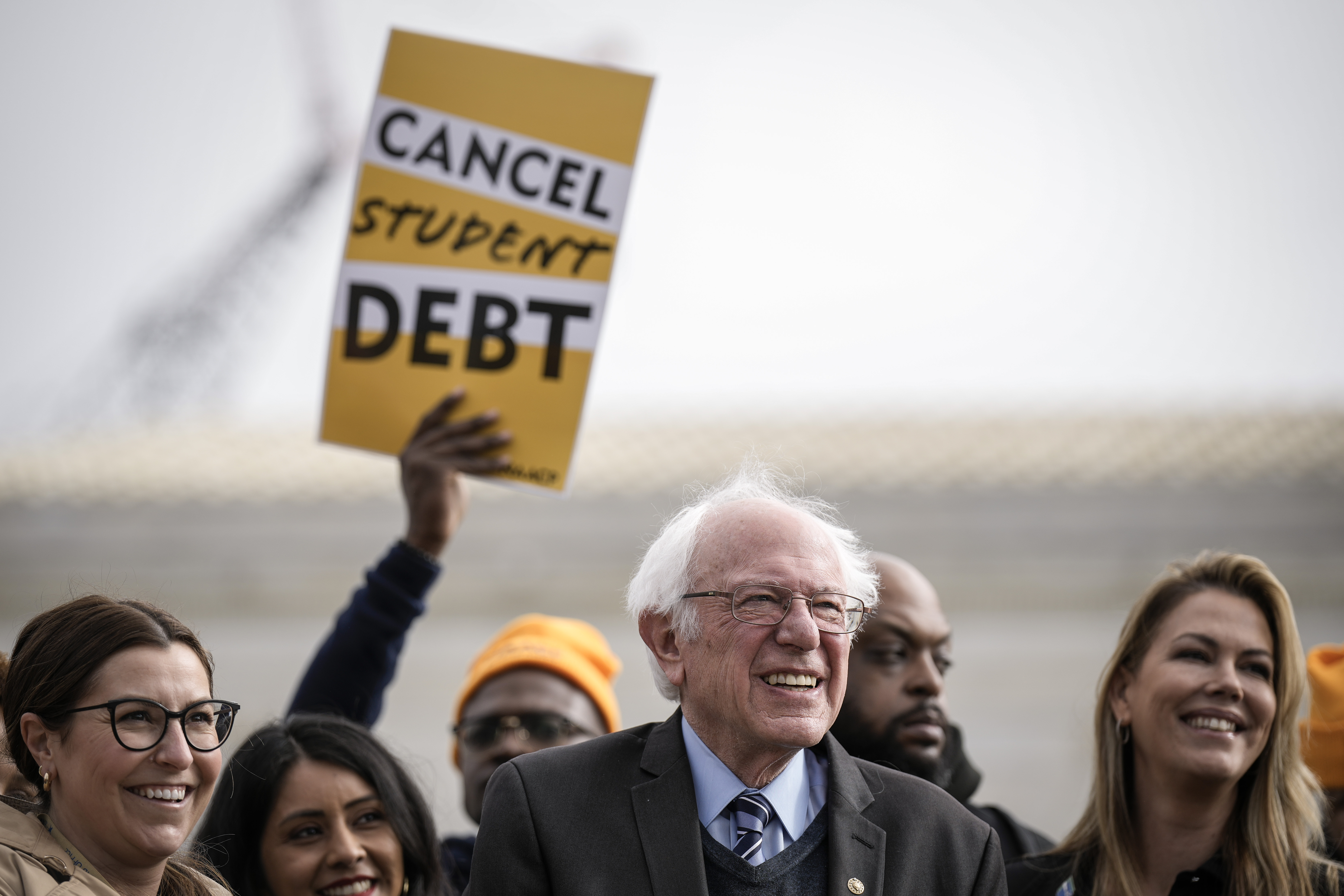Bernie Sanders in a crowd, one holding a sign that reads “cancel student debt.”