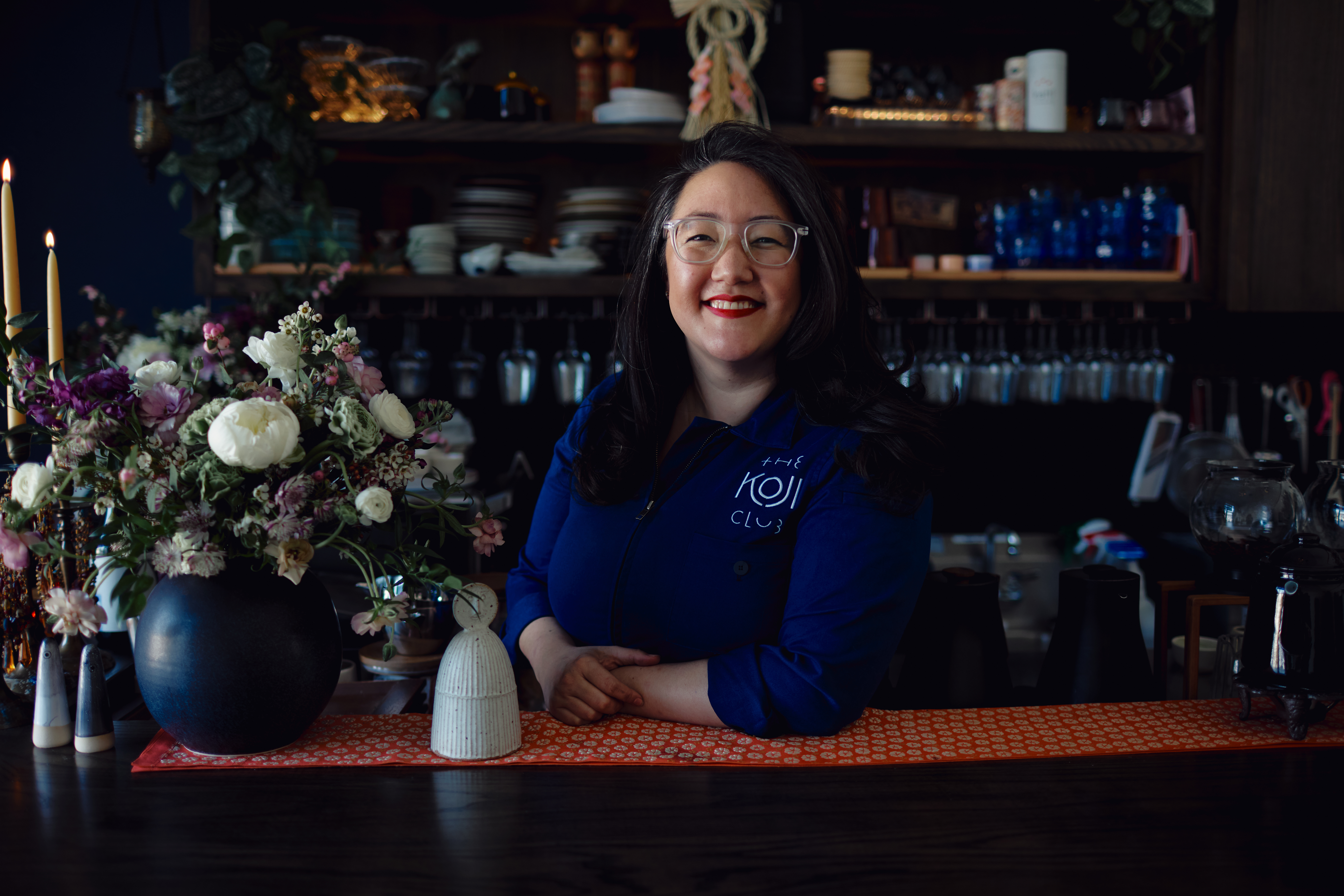 A woman stands smiling behind the sake bar for a portrait.