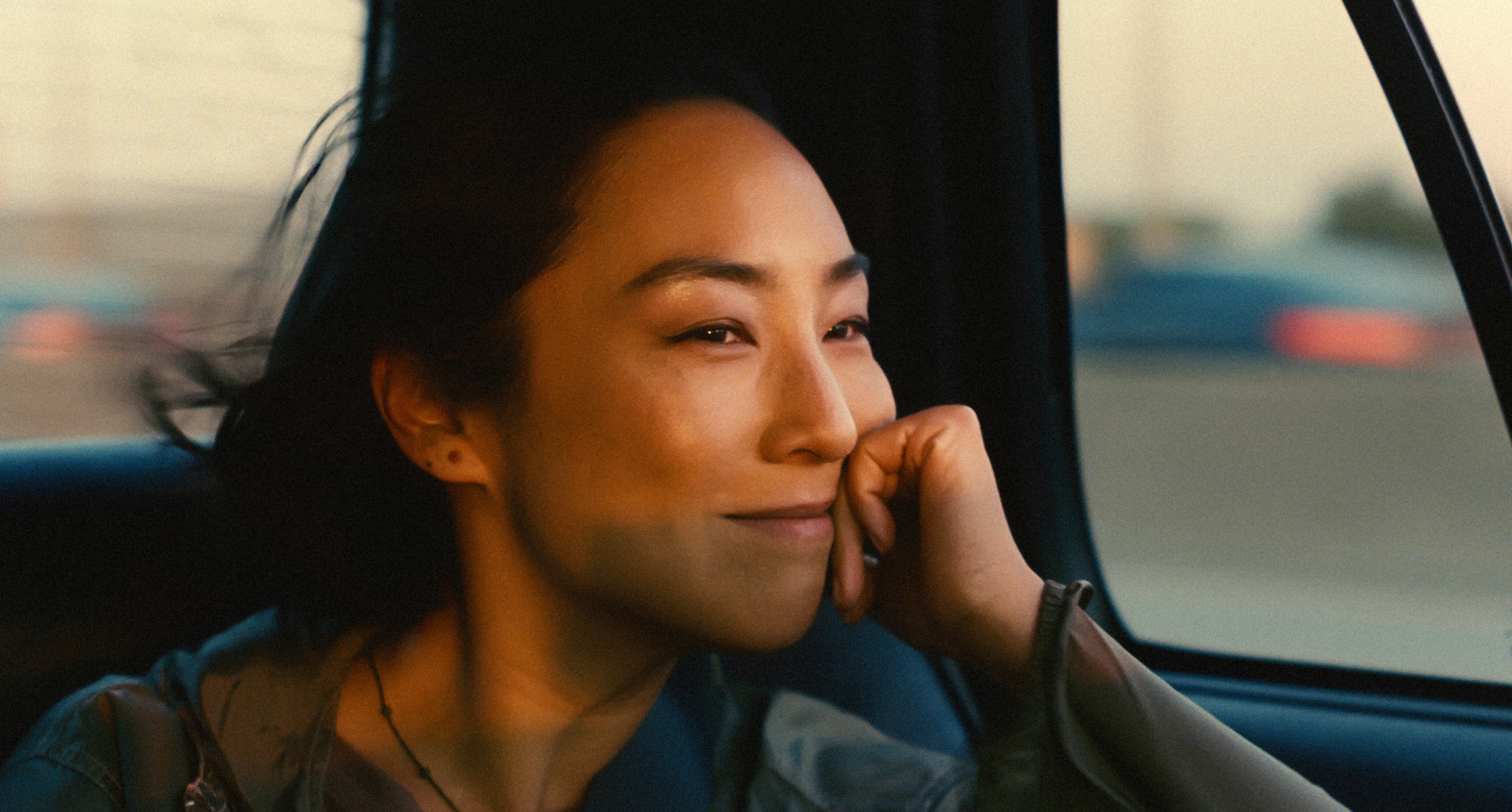 Asian woman smiles while holding her hand to her face sitting in a car.