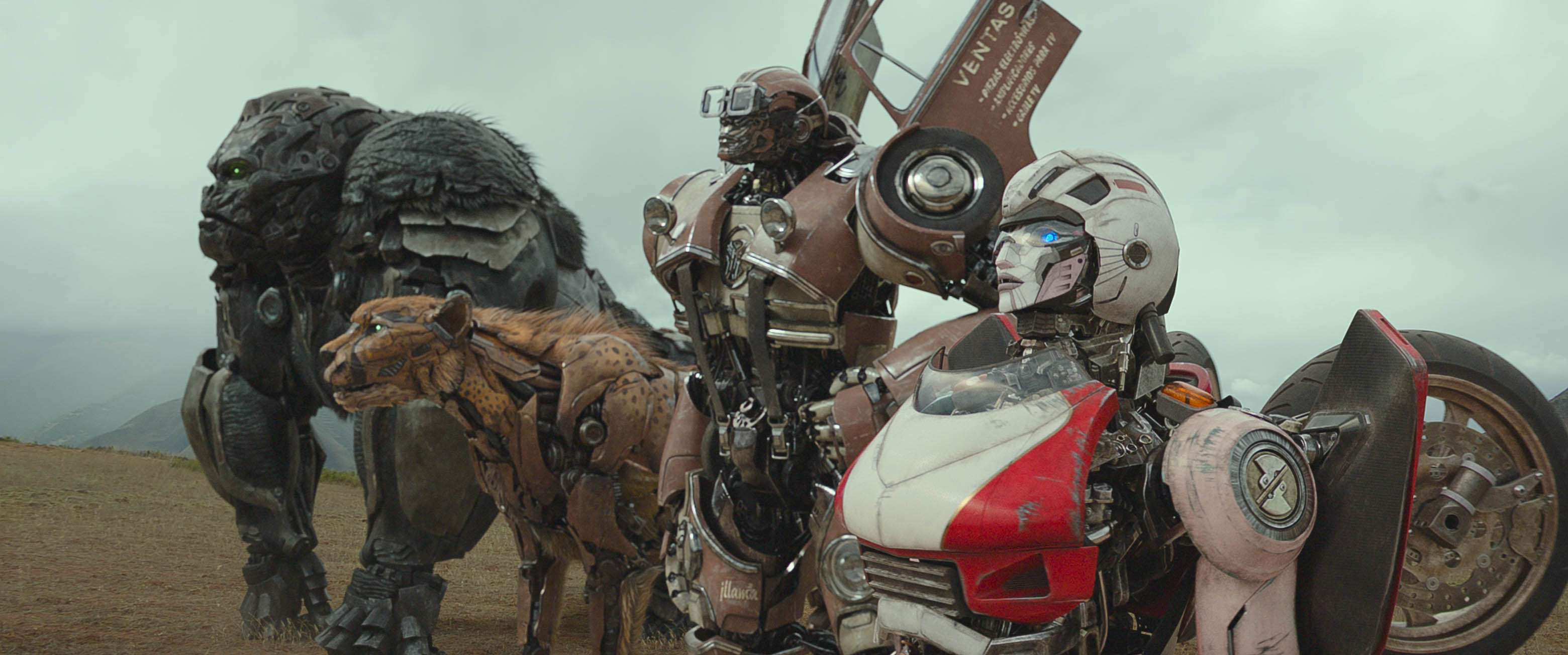 A group of sentient robots from Transformers: Rise of the Beasts (Optimus Primal, Cheetor, Wheeljack, and Arcee) stand together on a barren plain, facing off into the distance