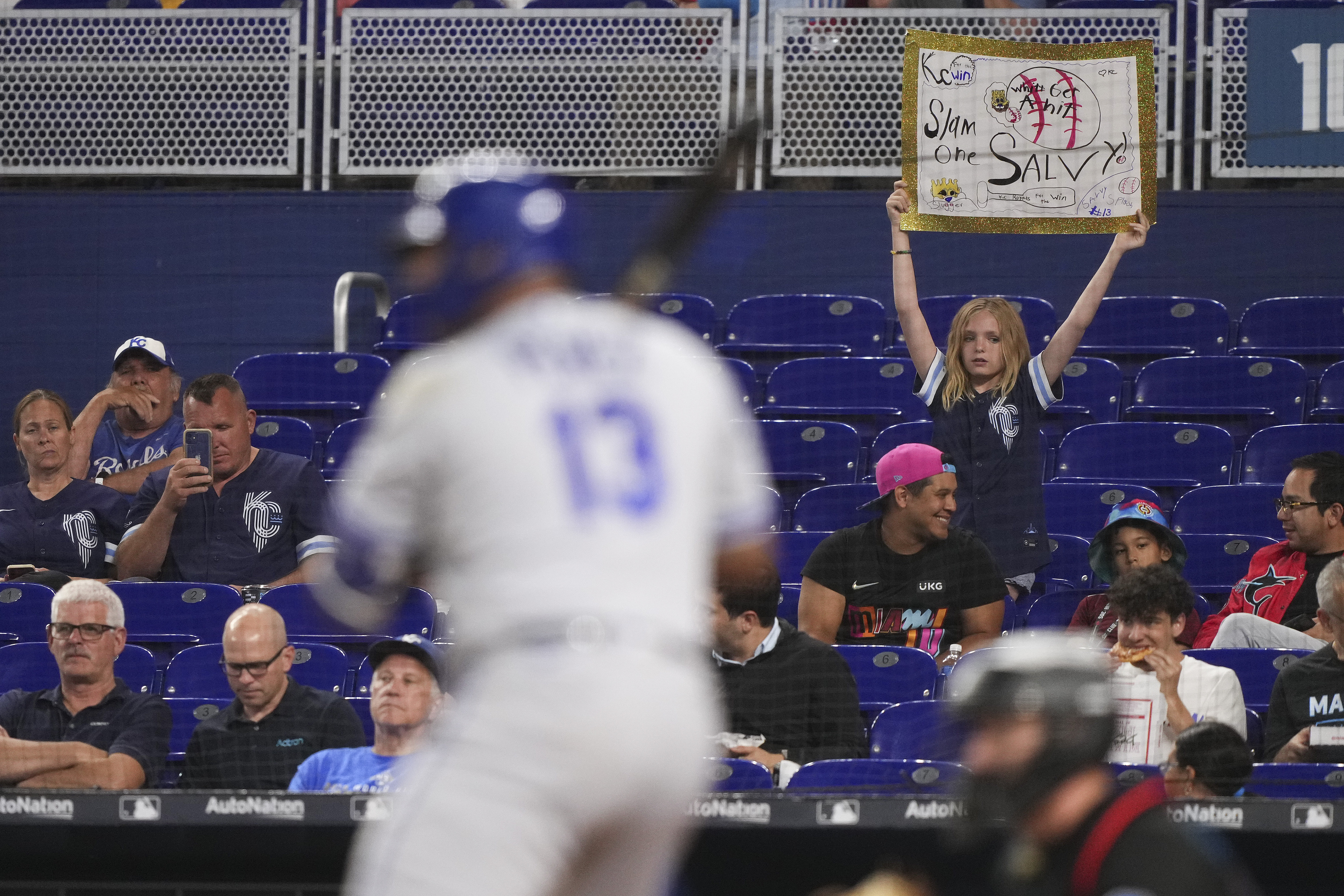 Salvador Perez stands at the plate while a fan holds a sign in the background