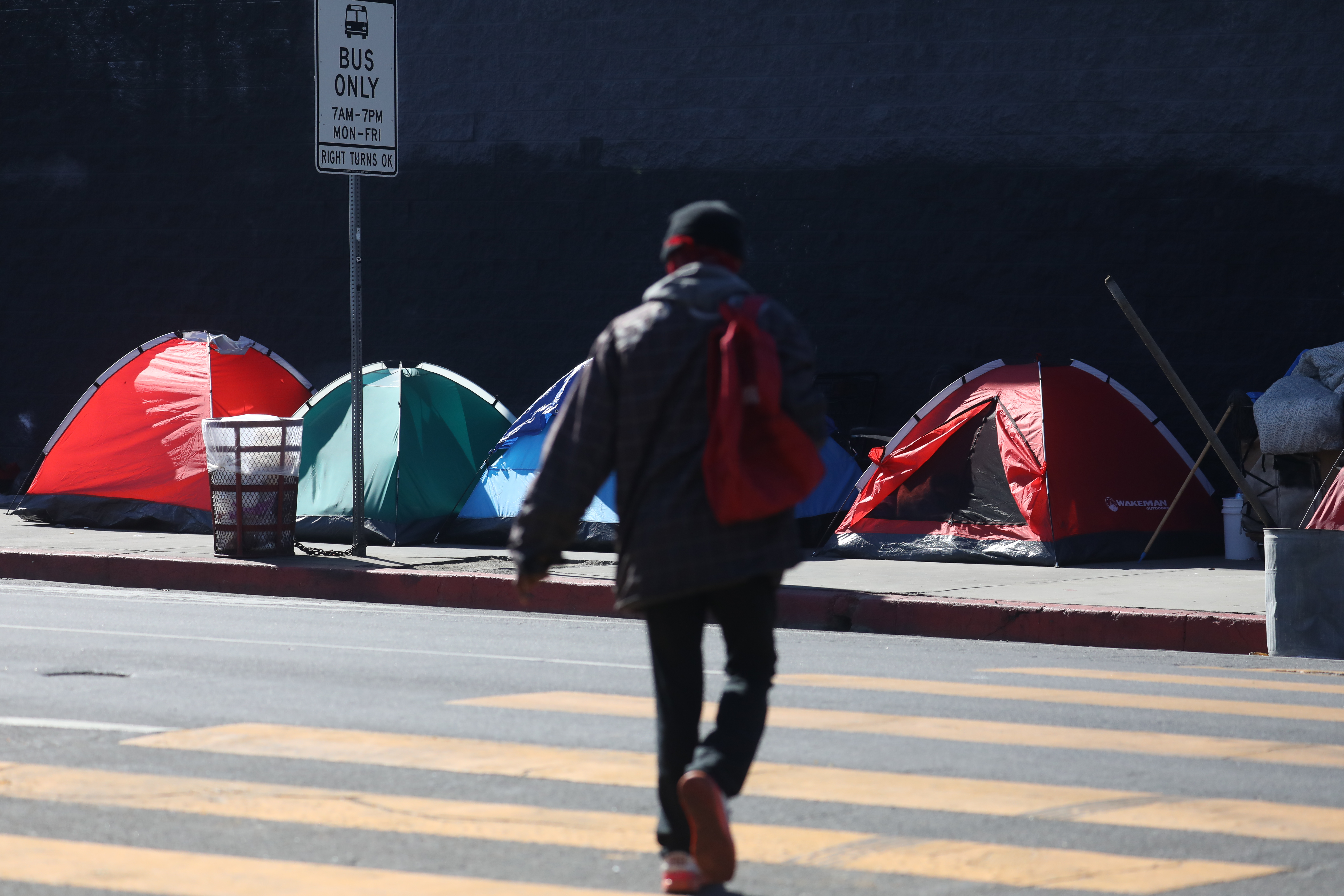 A person walking across a city street toward a row of tents.