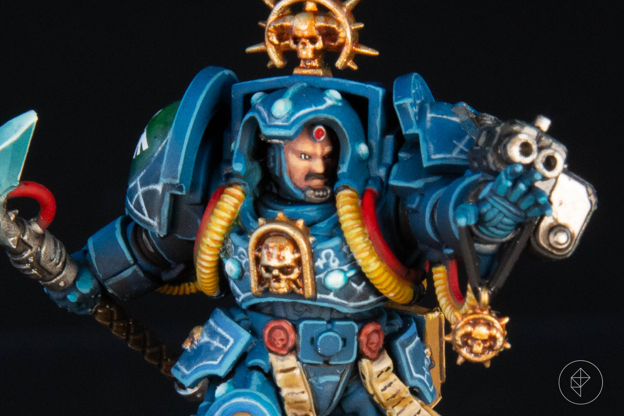 A Space Marine Terminator librarian, painted to a high level, stands ready to face a Tyranid. His armor is blue, and his hand is raised as if casting a spell.