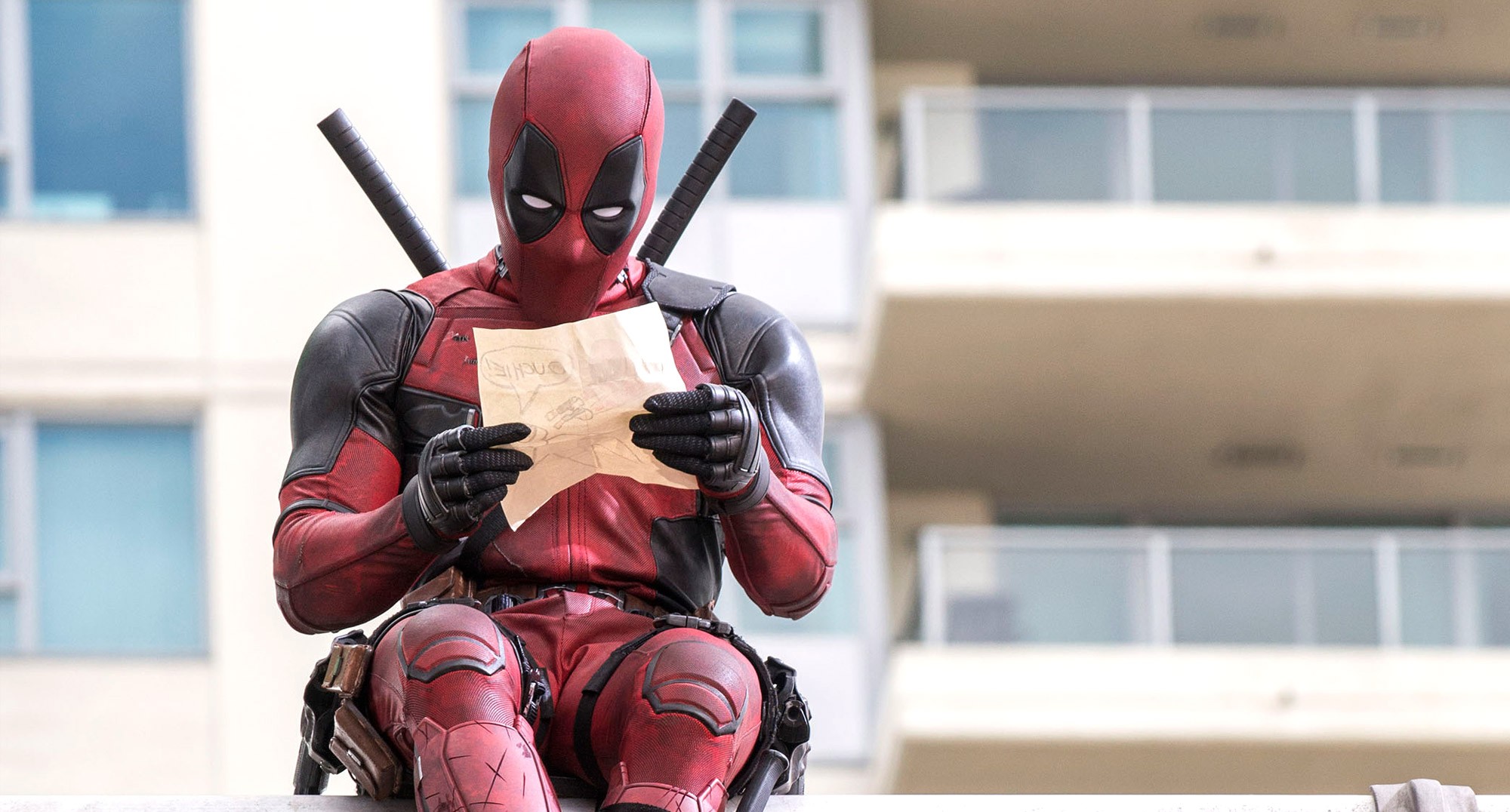 Deadpool reading a note while sitting on a highway.