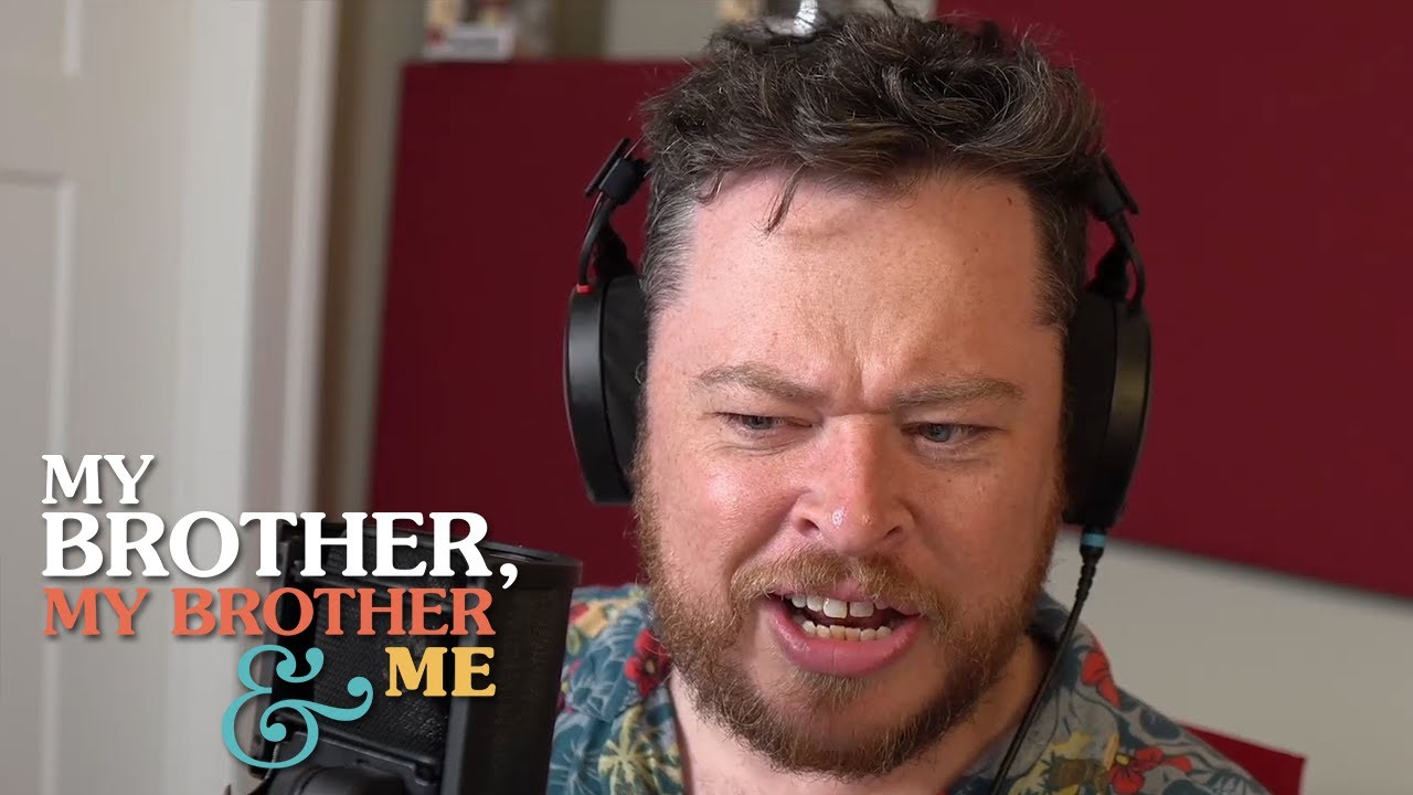 An image of Justin McElroy, wearing headphones and seated behind a microphone, looking confused. The logo for My Brother, My Brother and Me is superimposed over the photo in the lower left corner.