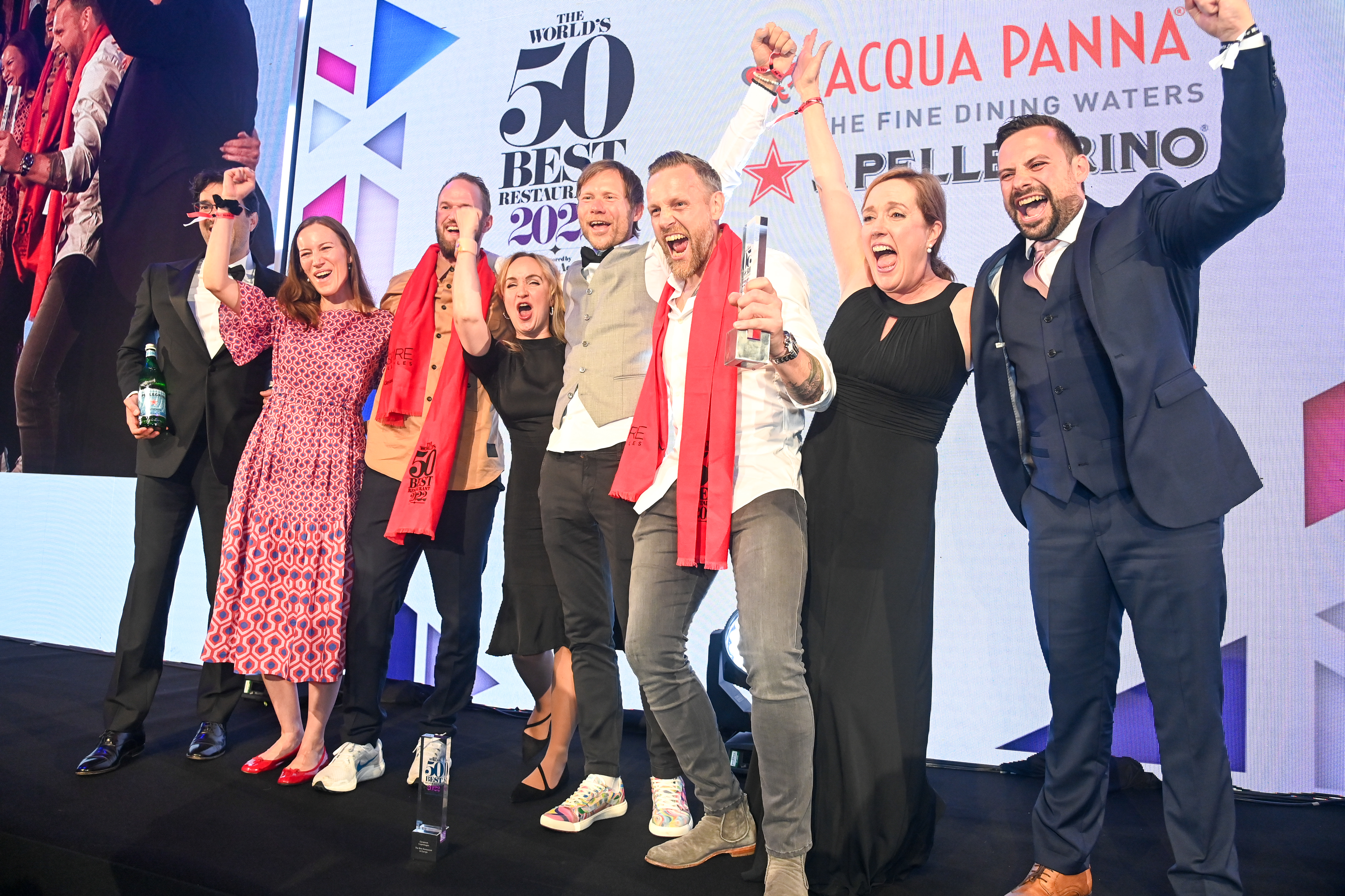 The Geranium team holds their arms up in victory in front of a screen featuring the World’s 50 Best logo.