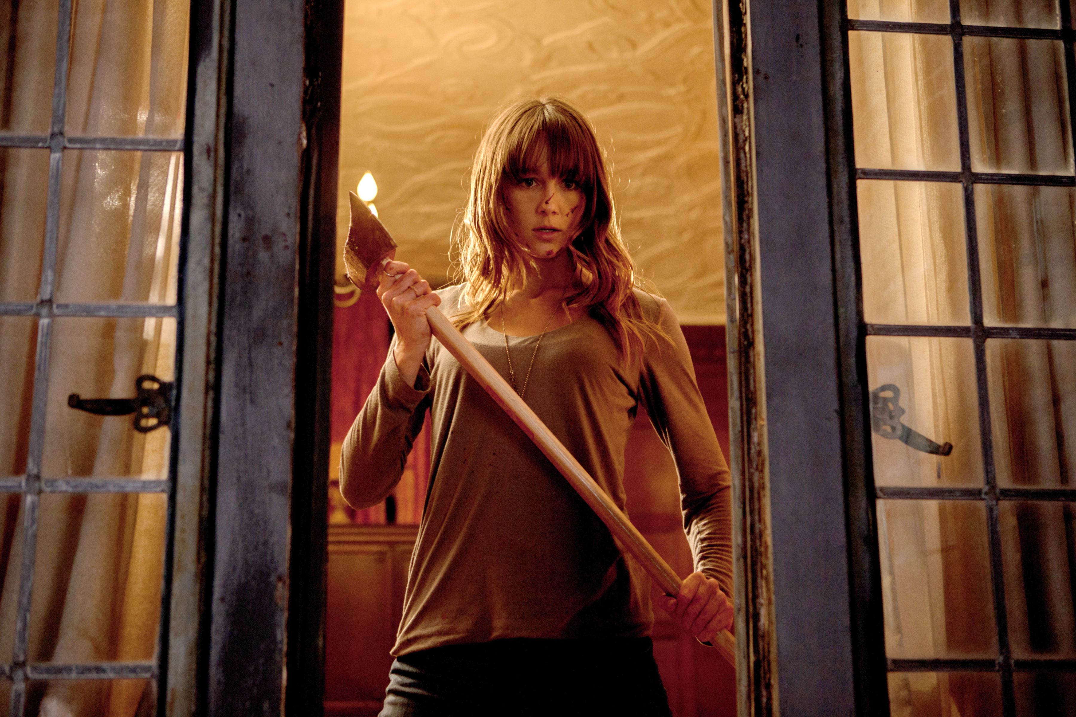 Sharni Vinson in You’re Next seen through a broken window holding an ax covered in blood