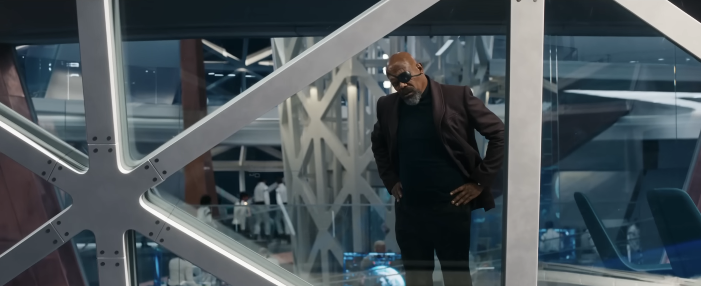 Nick Fury looks out a window framed by metal struts on the SABER space station. He looks frustrated. From a trailer for The Marvels. 