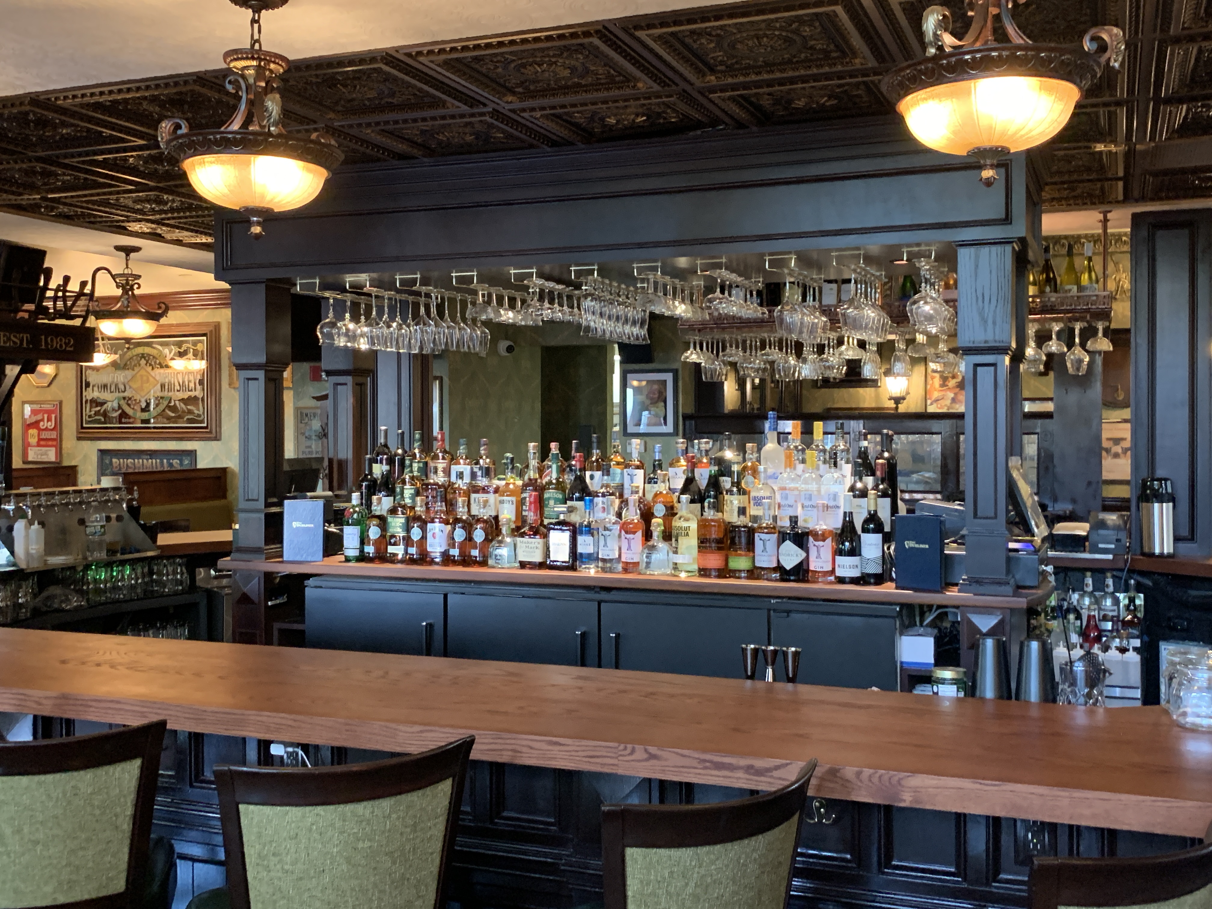 A bar with empty barstools lined against a wooden countertop and liquor bottles lining the back wall behind the bar.