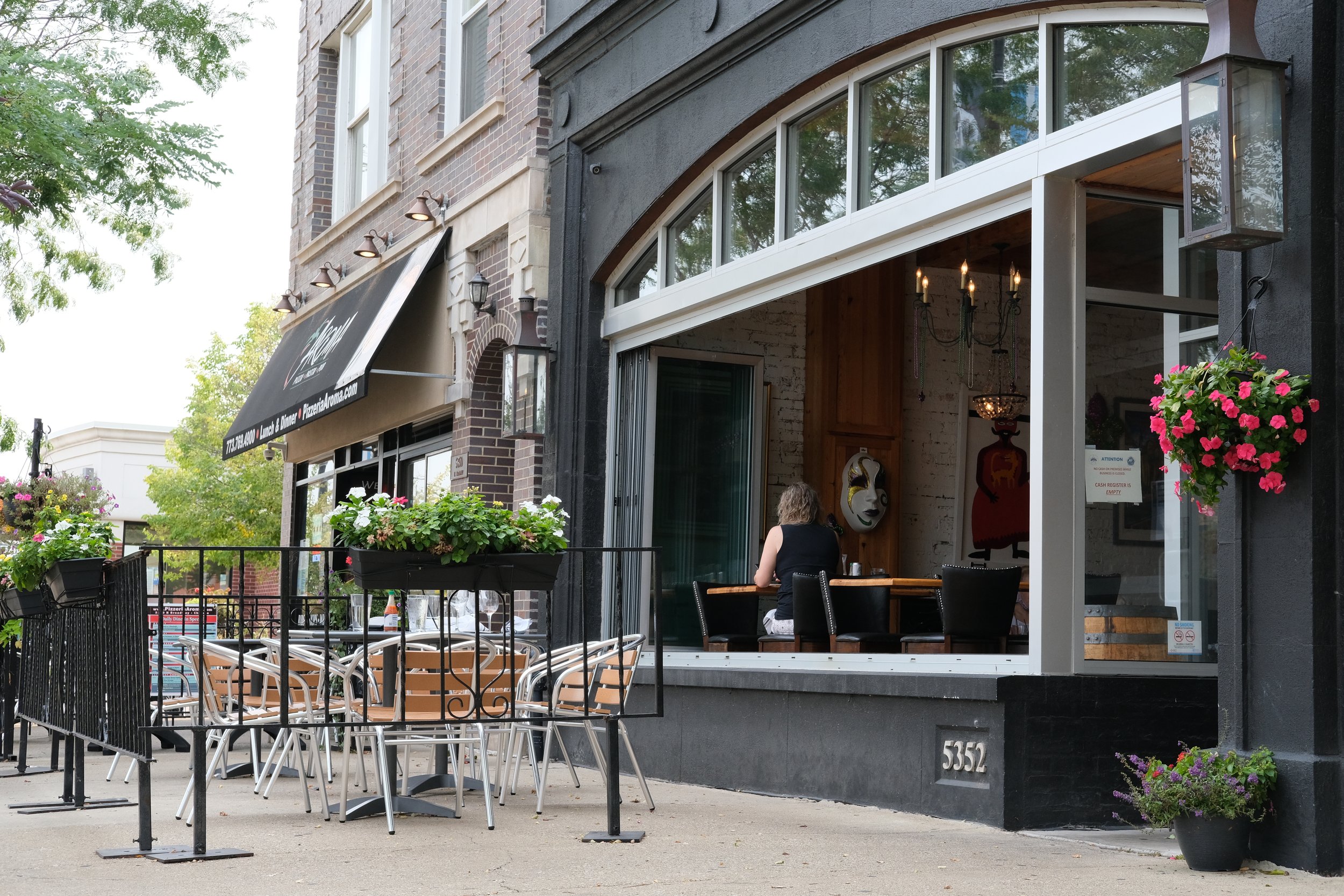 A black storefront restaurant with an open window facing a sidewalk patio.