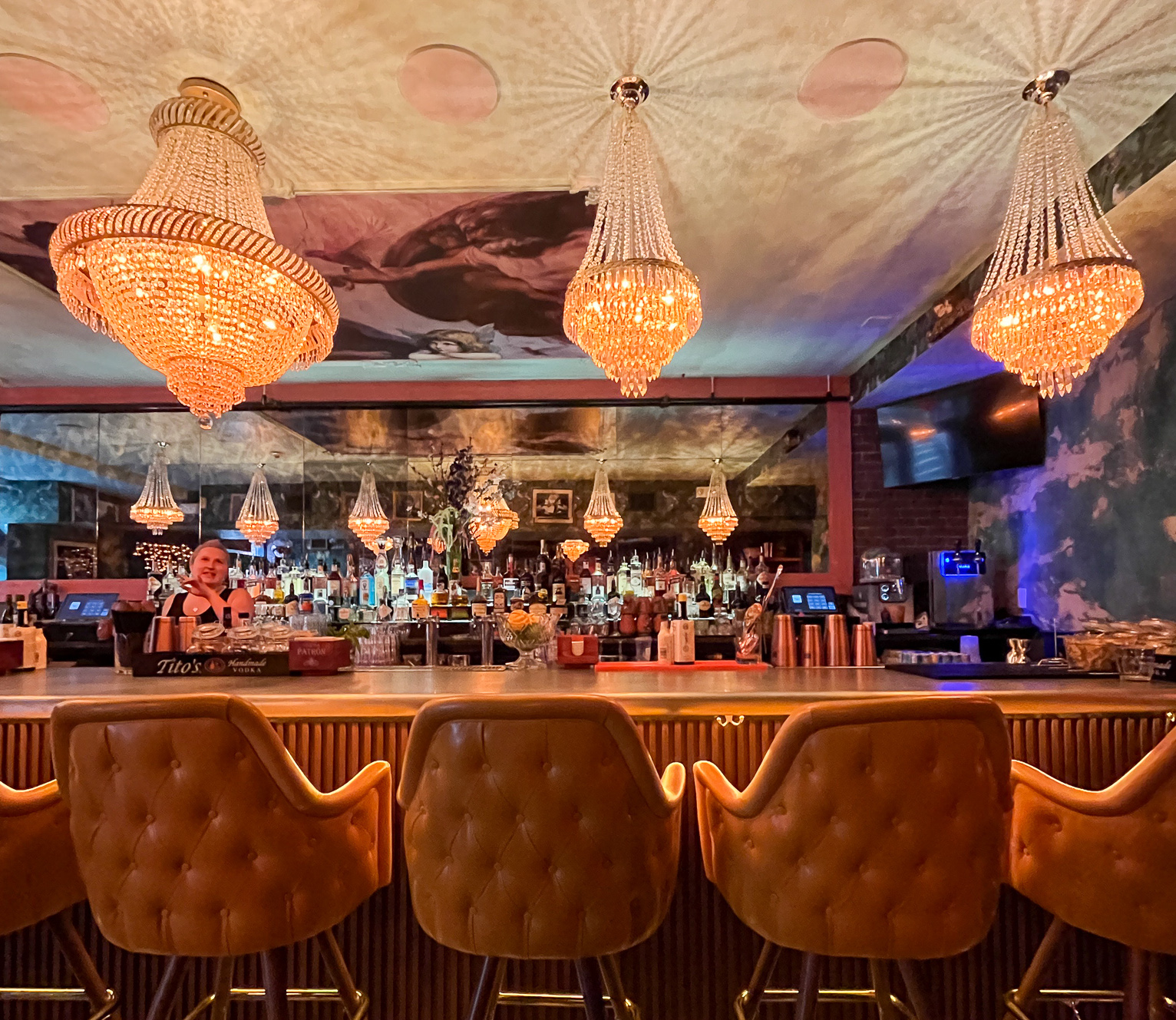 A golden-hued bar with sparkly chandeliers hanging above and a mirror against the back wall.