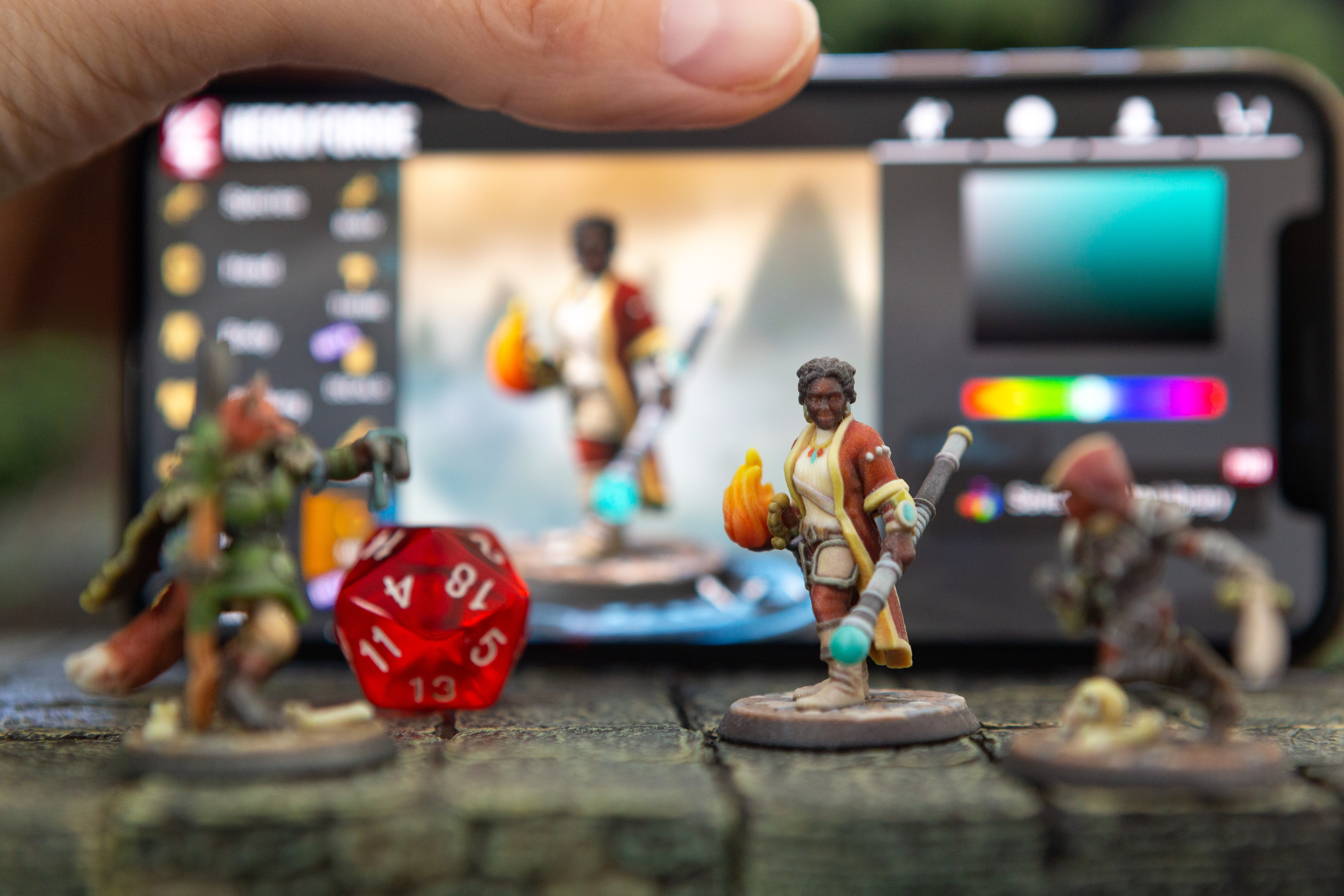 Several color-printed miniatures stand in front of a cell phone, which is running the Hero Forge customization software