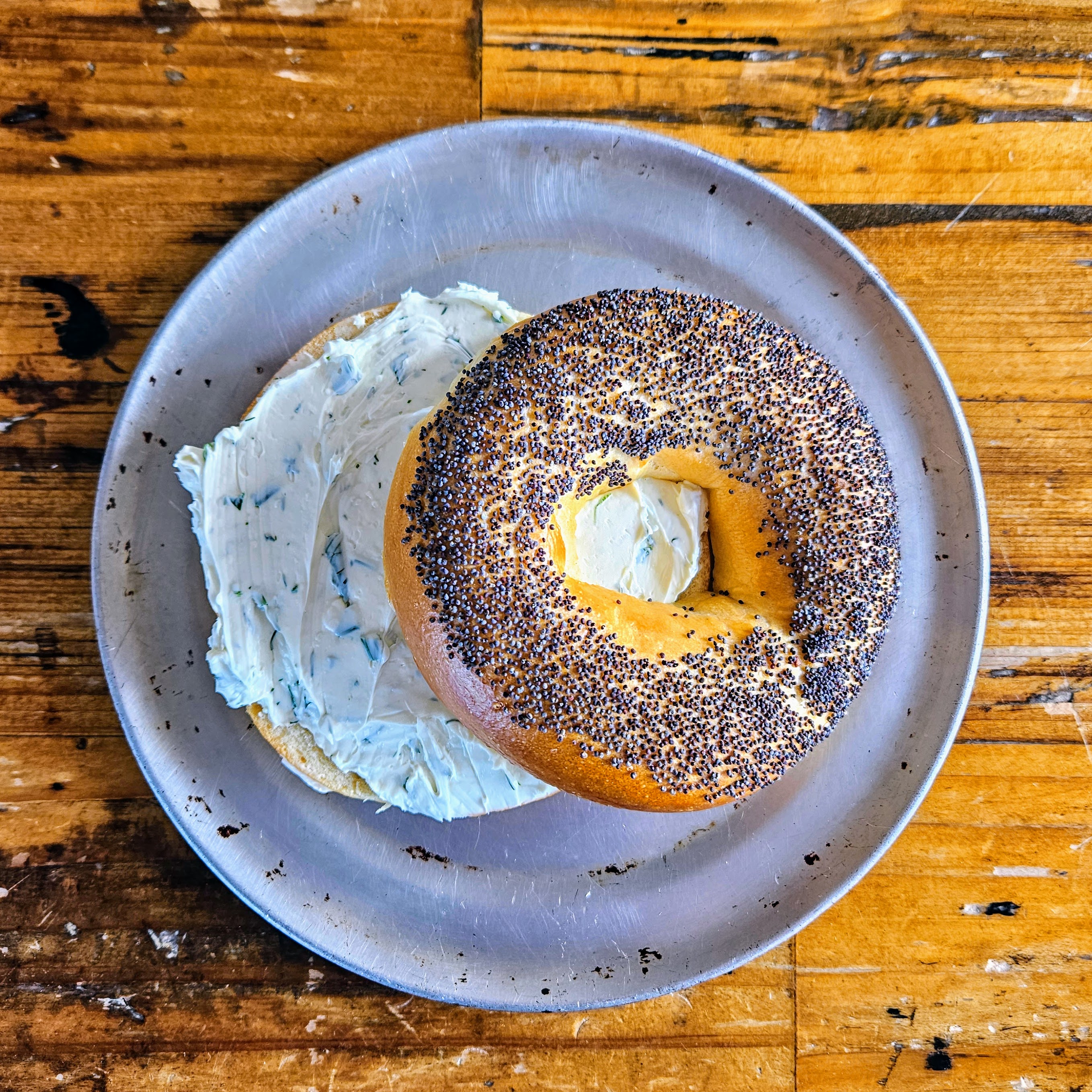 A bagel with cream cheese on a round metal plate.