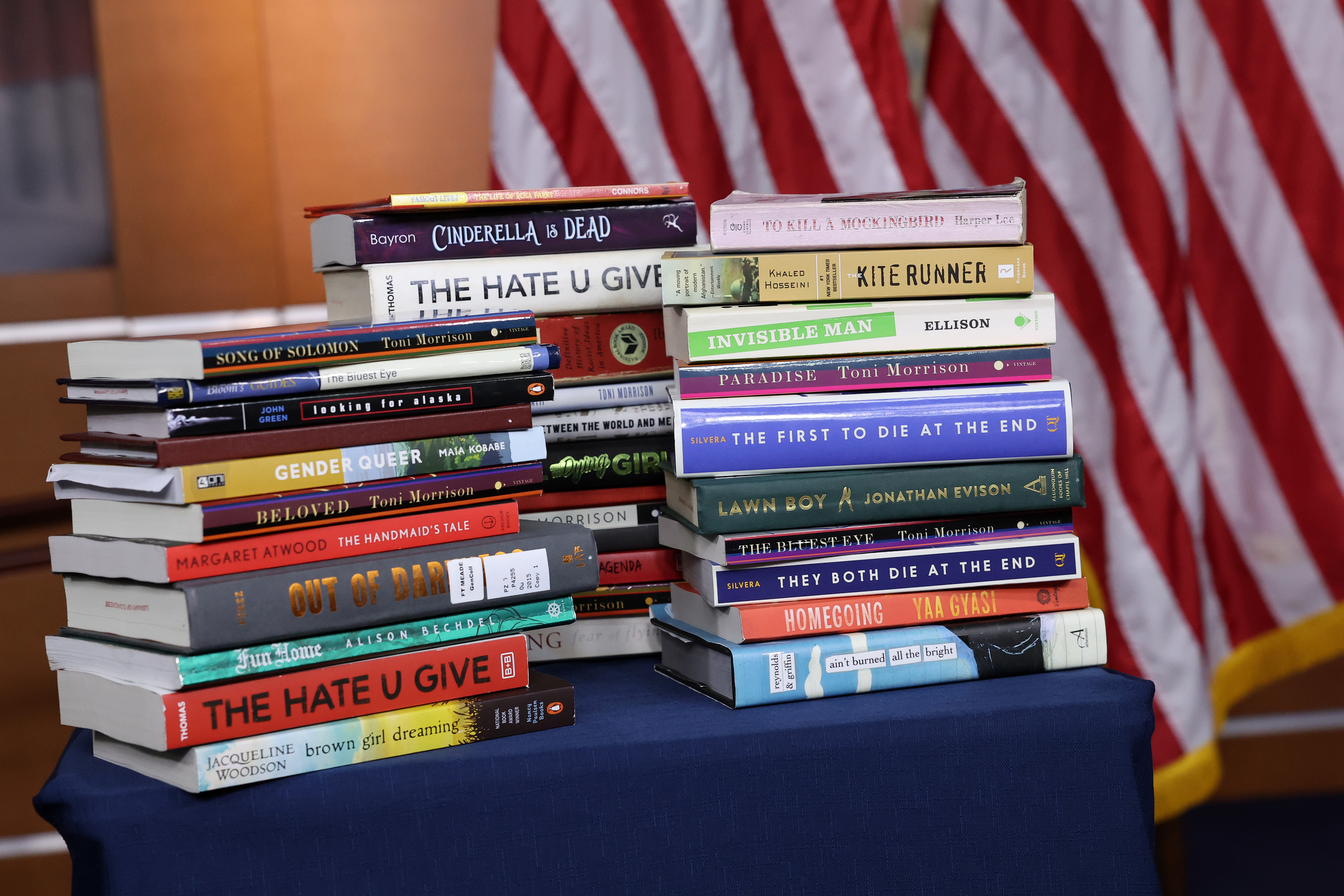 Books stacked on a table with an American flag in the background. 