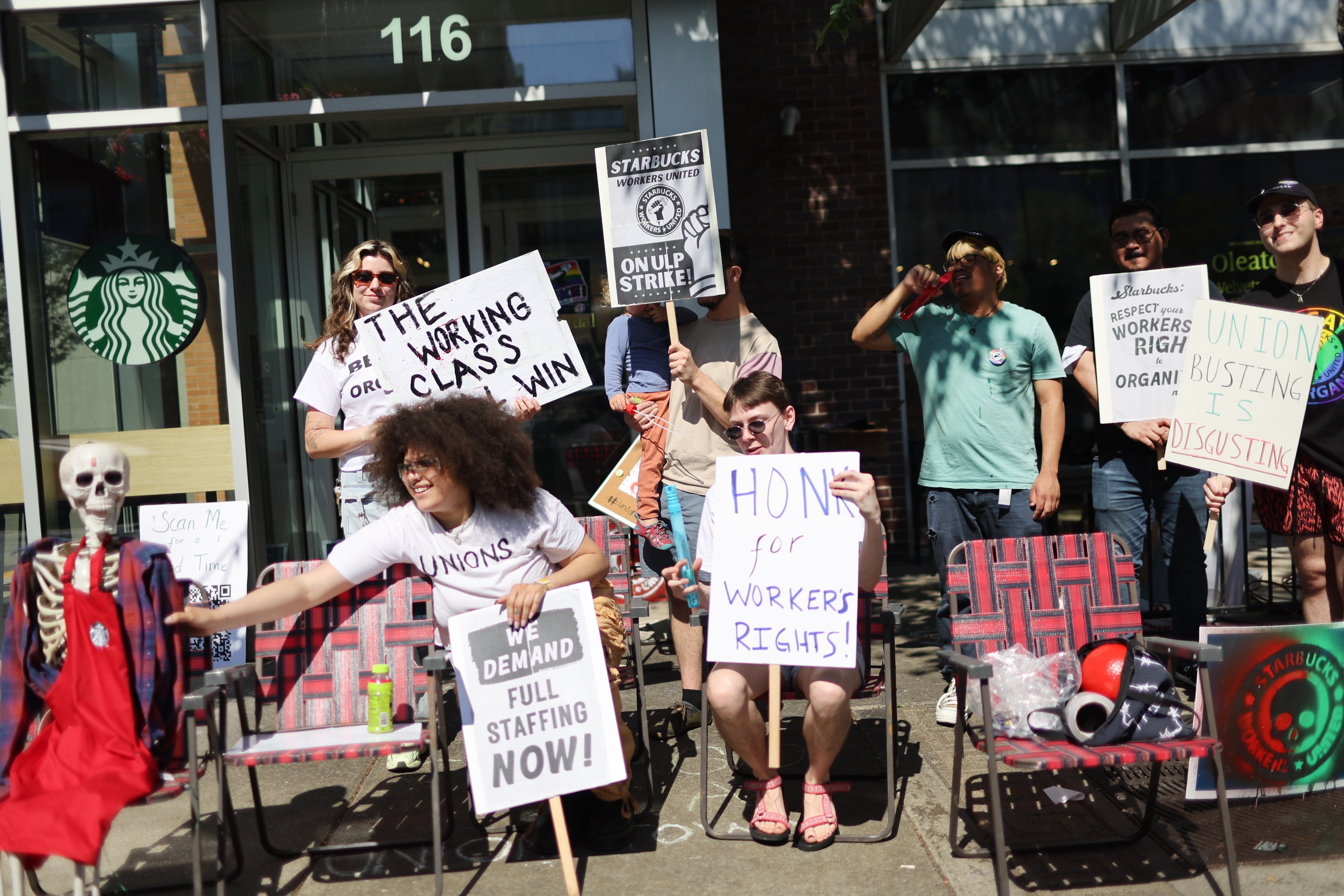 A group of people with protest signs demanding fair pay in front of a Starbucks