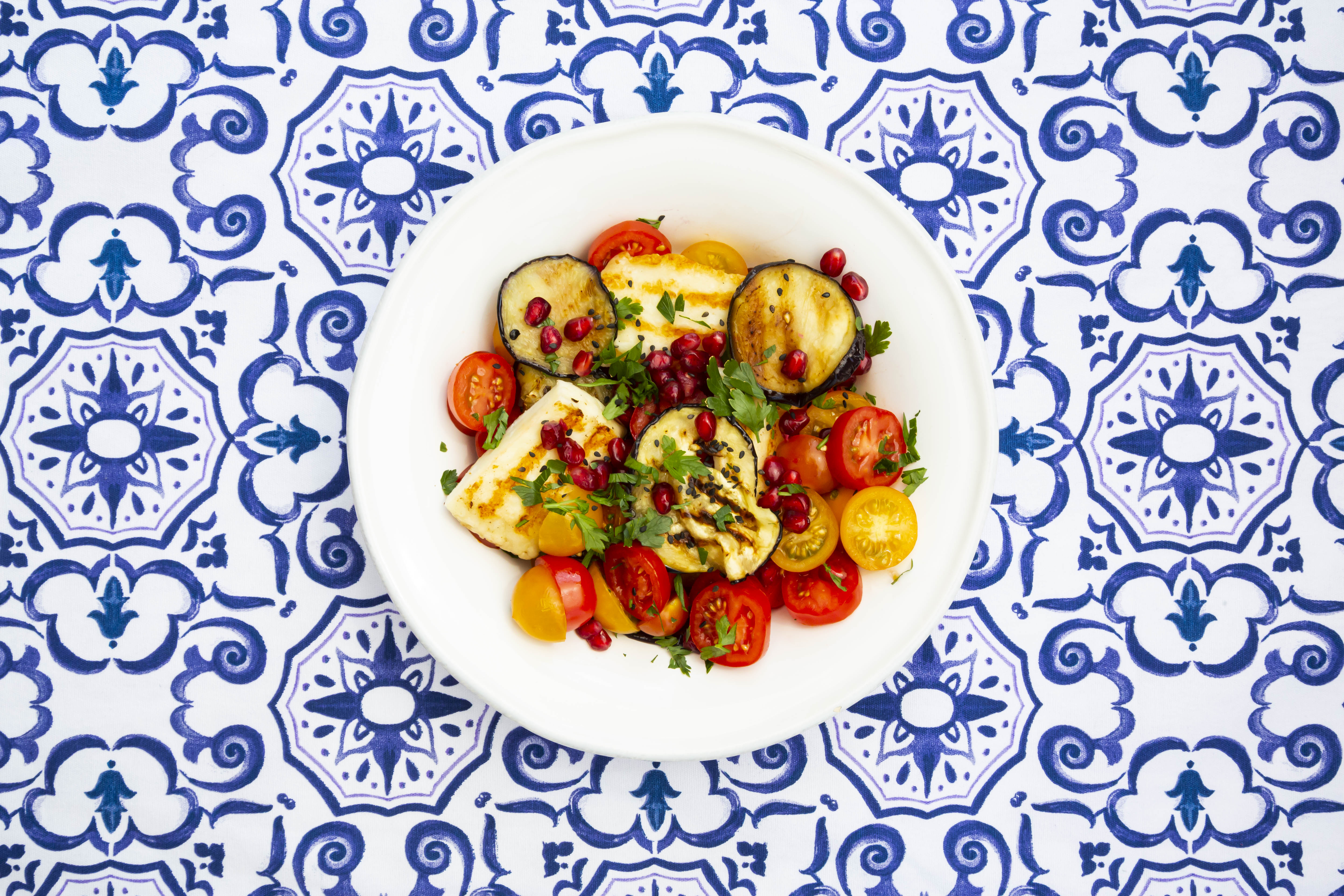 A plate of zucchini, tomato, and halloumi salad, set on blue and white tiles.