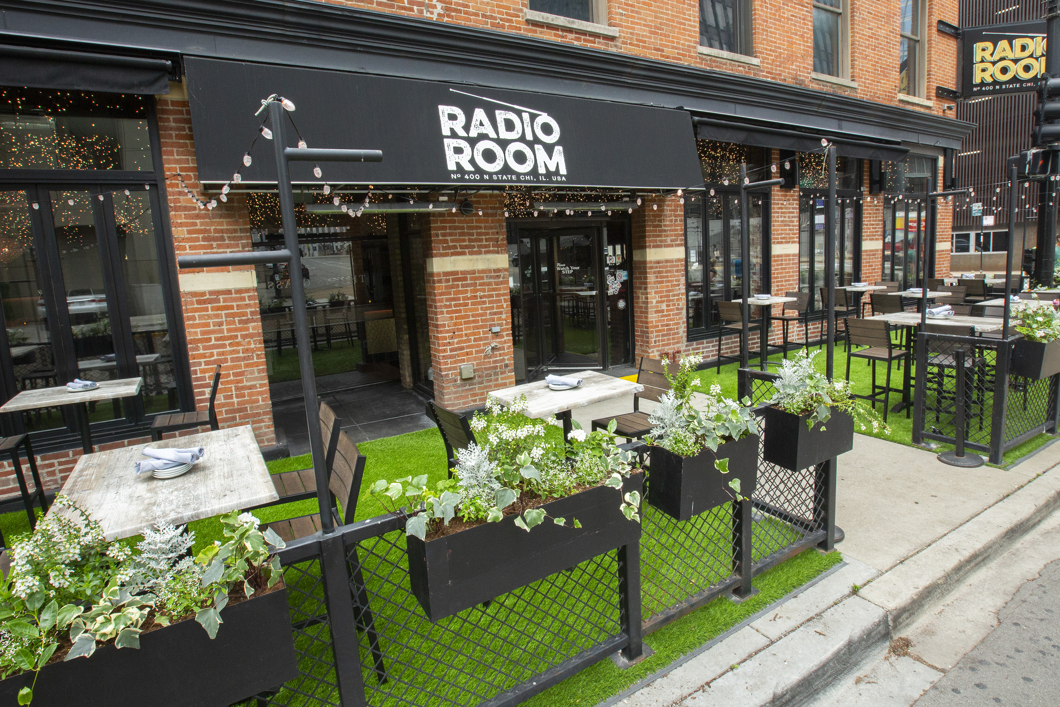 A grassy patio in front of a restaurant entrance with black awning that reads “Radio Room.”