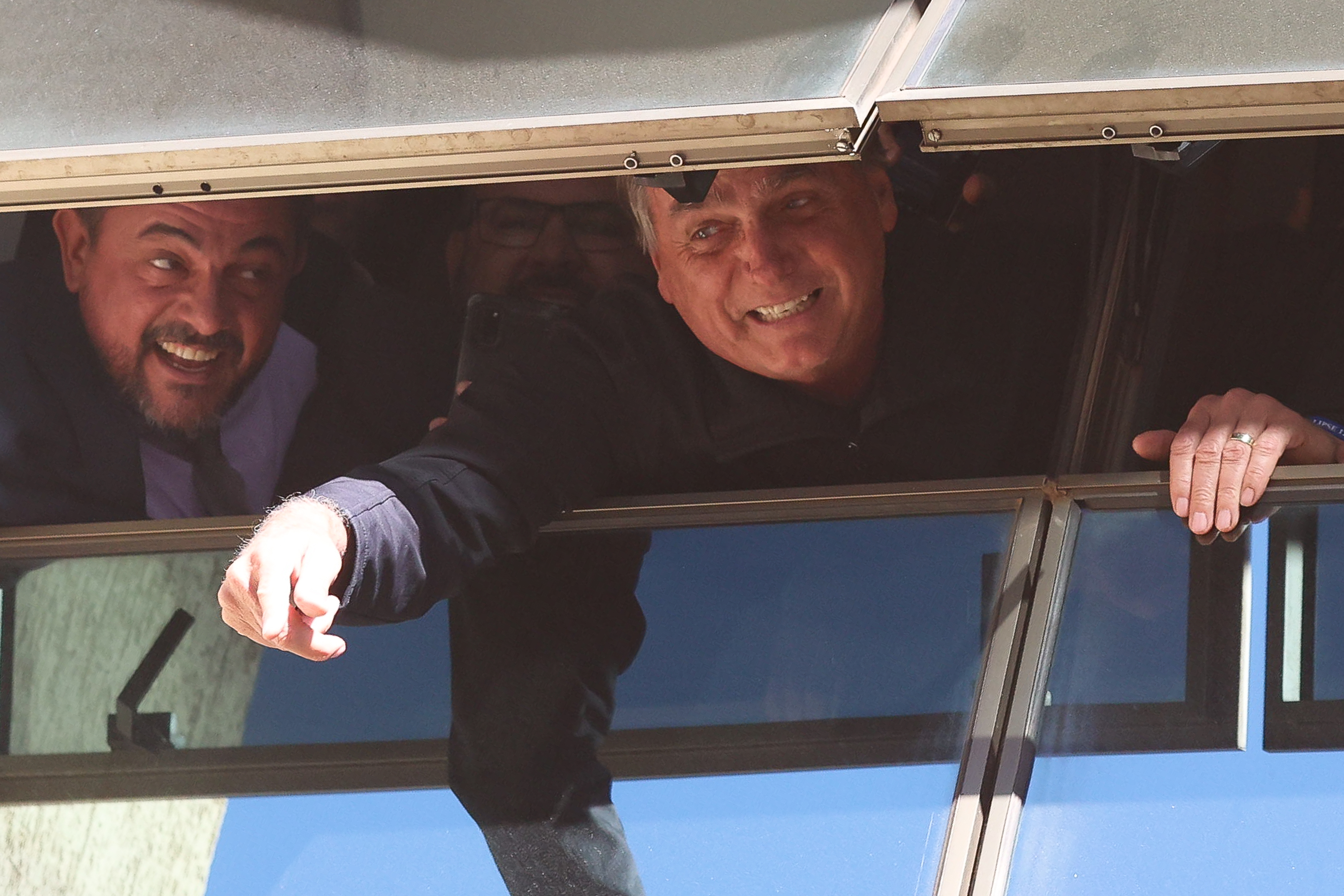 Jair Bolsonaro, smiling broadly, reaches his hand out of an open window.