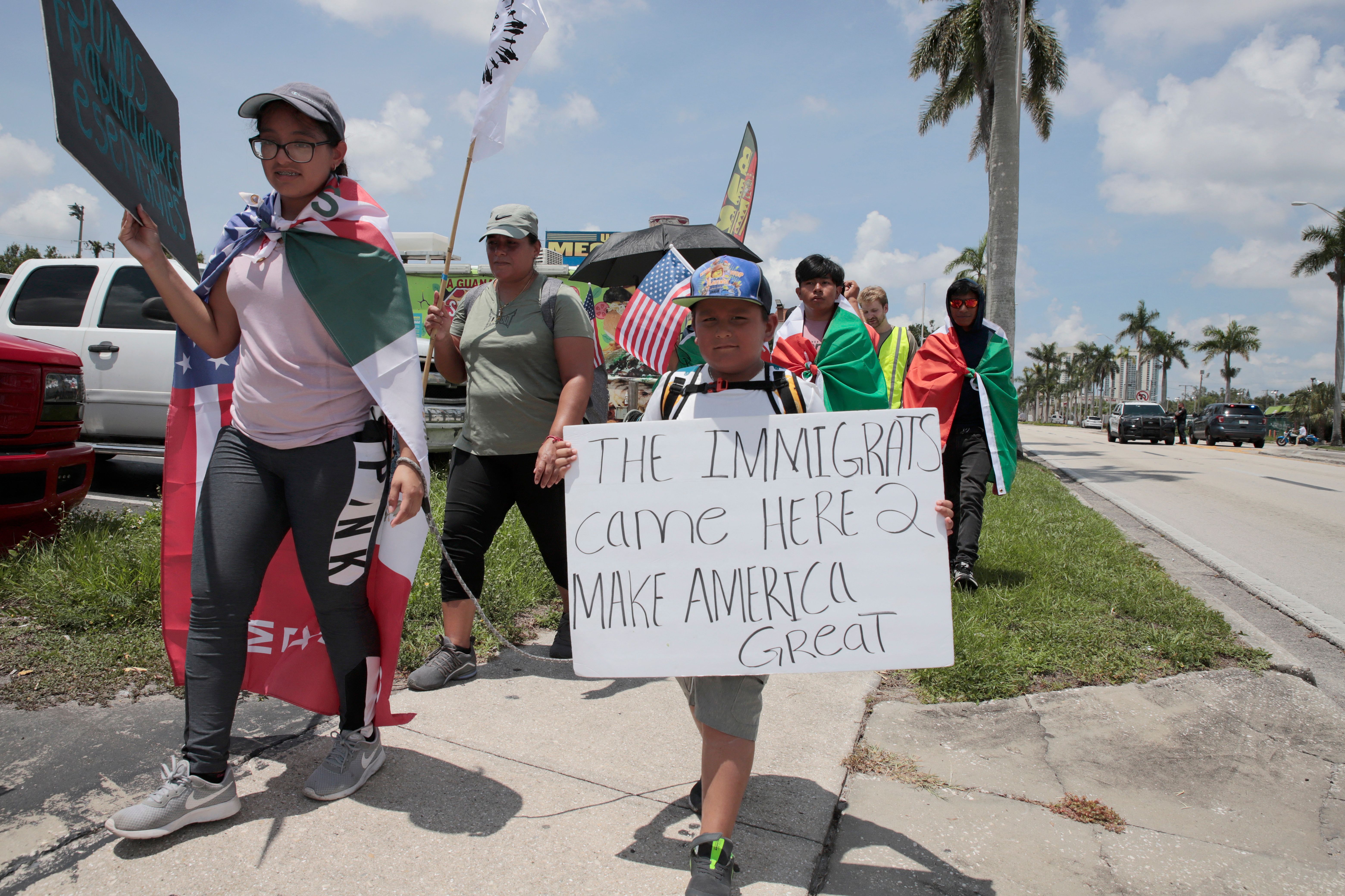 A protester walking with a group along a Florida road carries a sign that reads, “The immigrants came here to make America great.”