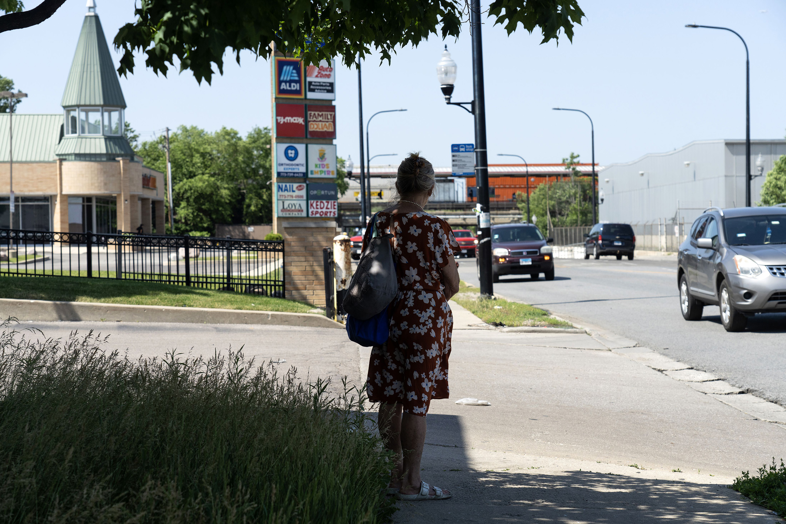 A commuter in Chicago stands in the shade waiting for her bus.