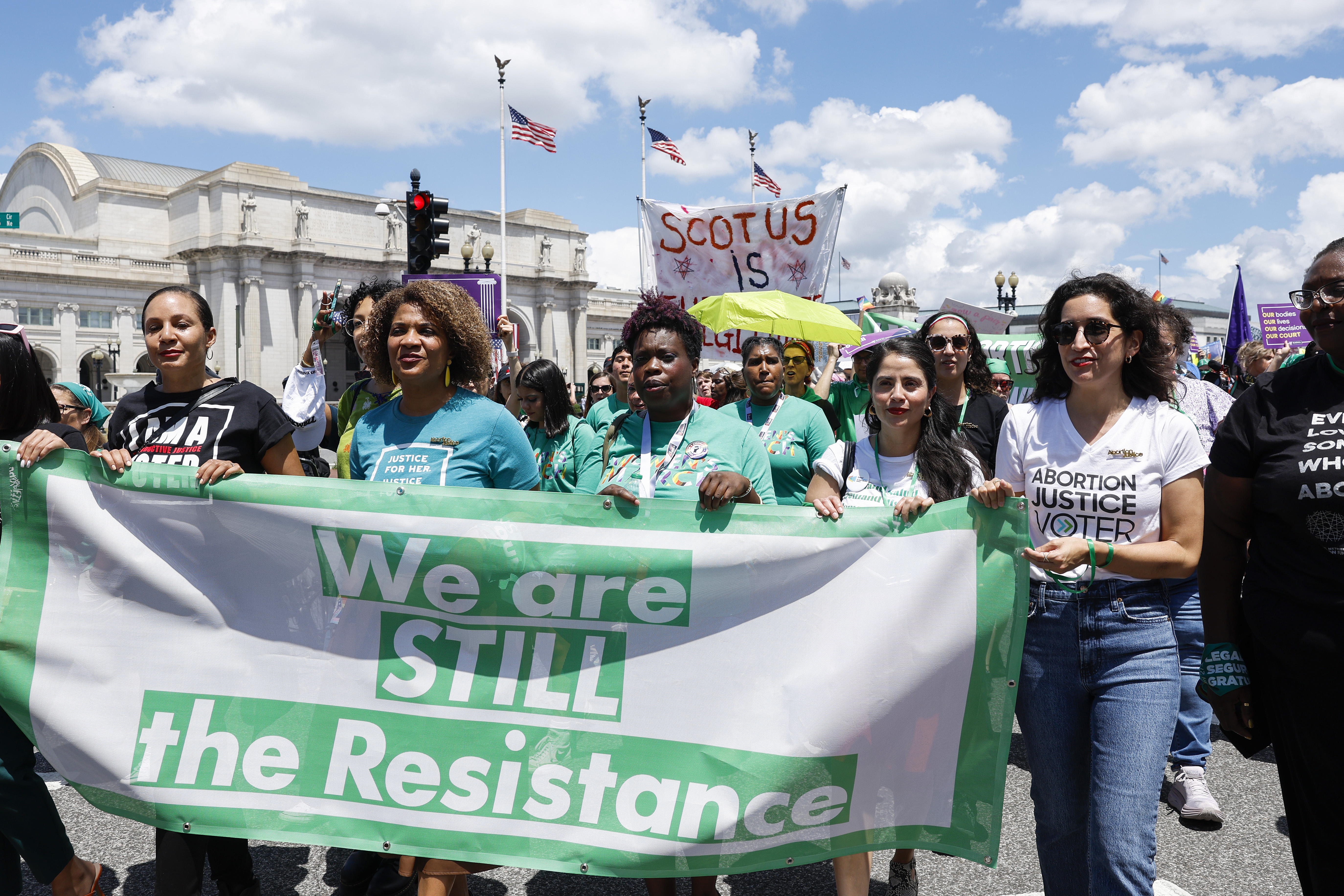 Abortion rights activists hold a large white and green banner with the words: We are STILL the Resistance.