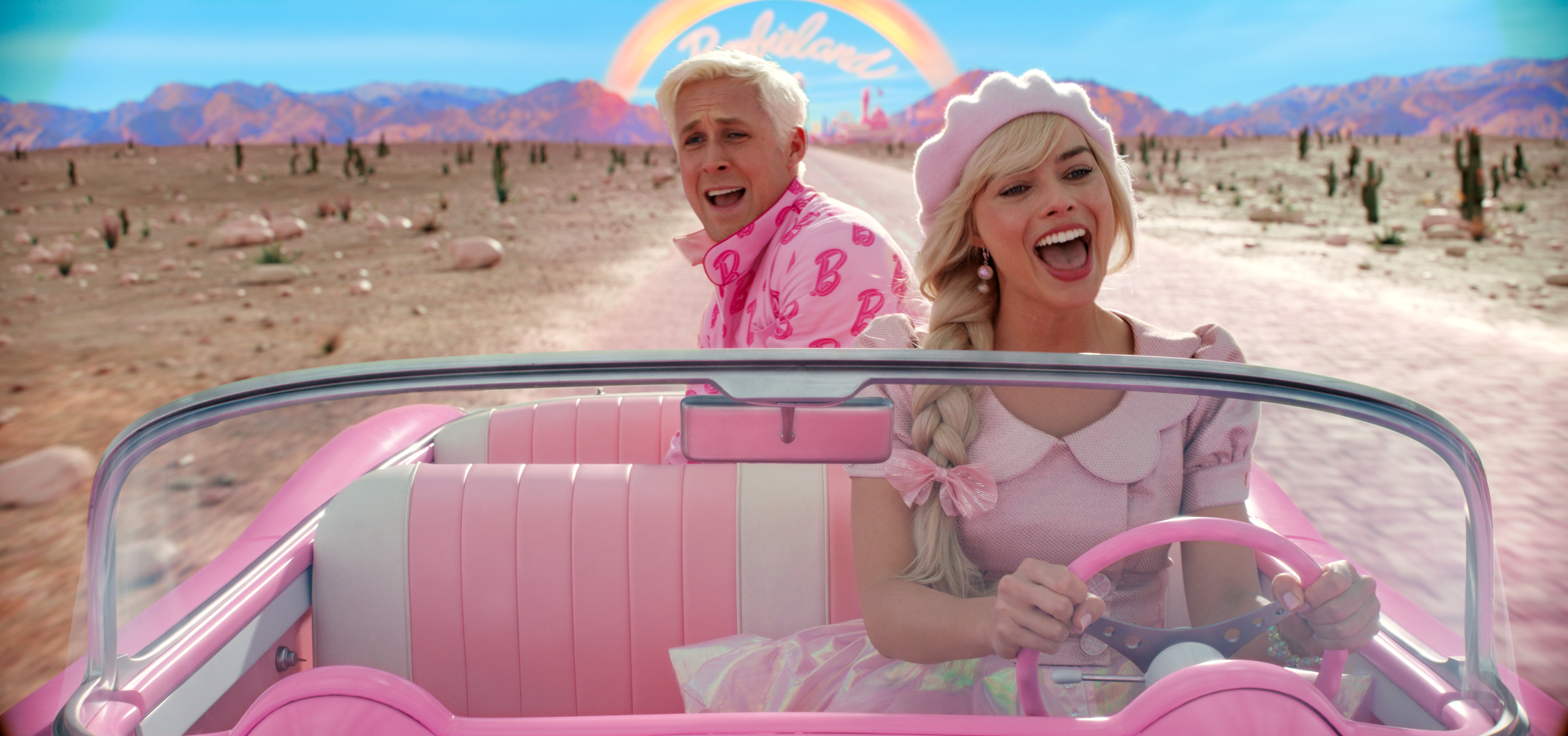 A woman in pink driving a pink convertible car with a man in pink in the backseat.