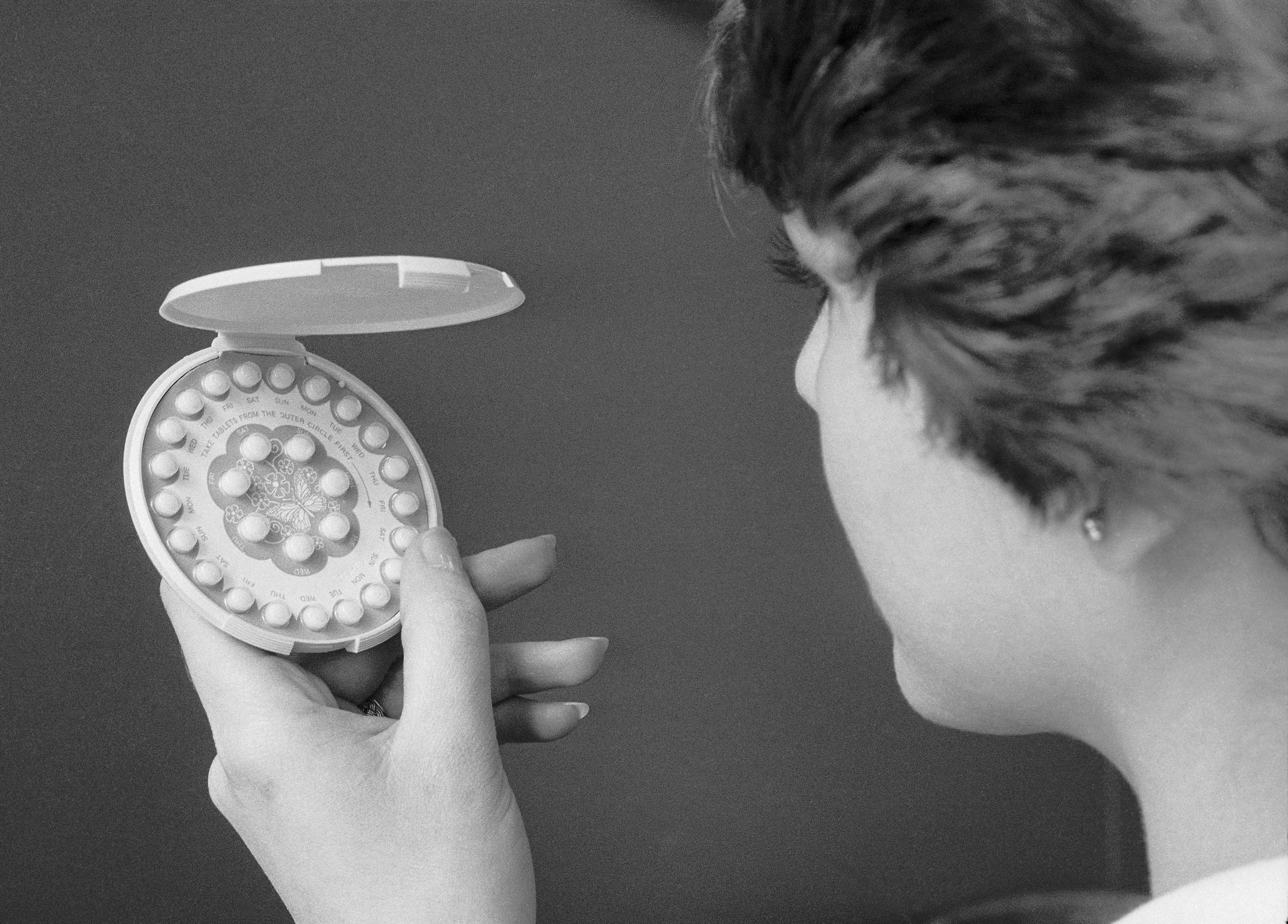A woman holding and looking at an open circular pill dispenser.