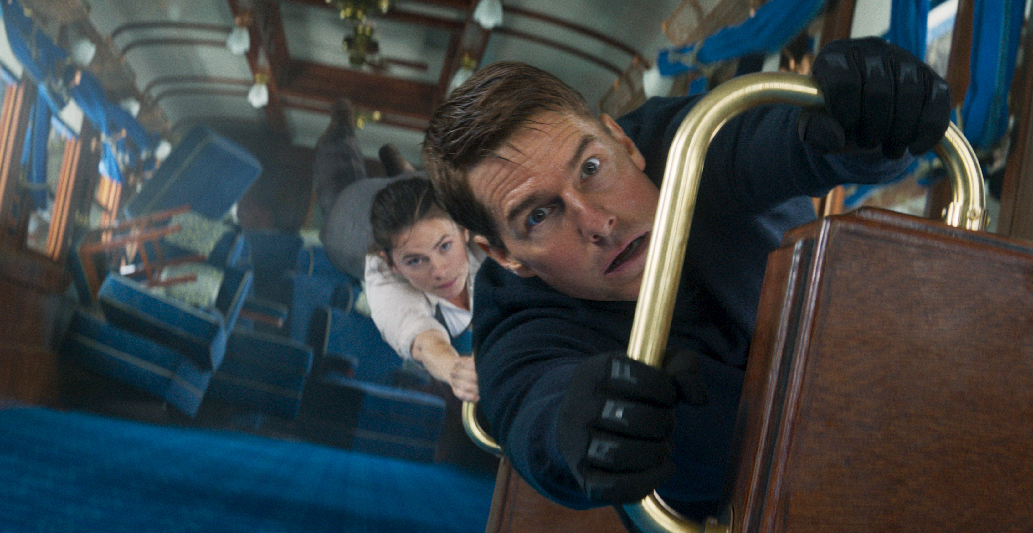 Tom Cruise as Ethan Hunt holds on to a railing in a train car turned vertical as Hayley Atwell clings on to him in Mission: Impossible — Dead Reckoning Part One