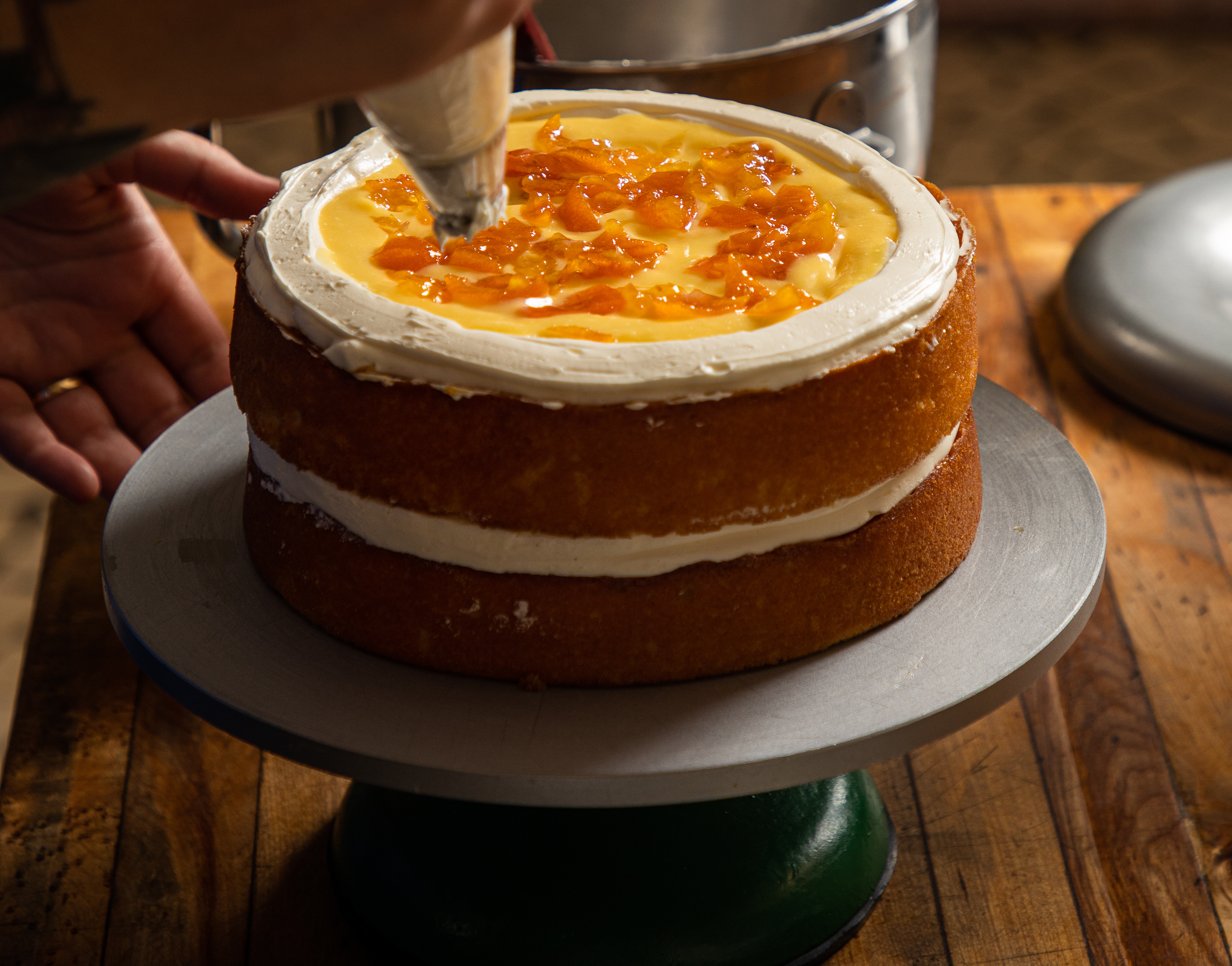 A two-layer cake topped with curd and preserved kumquats gets a layer of white icing piped on.