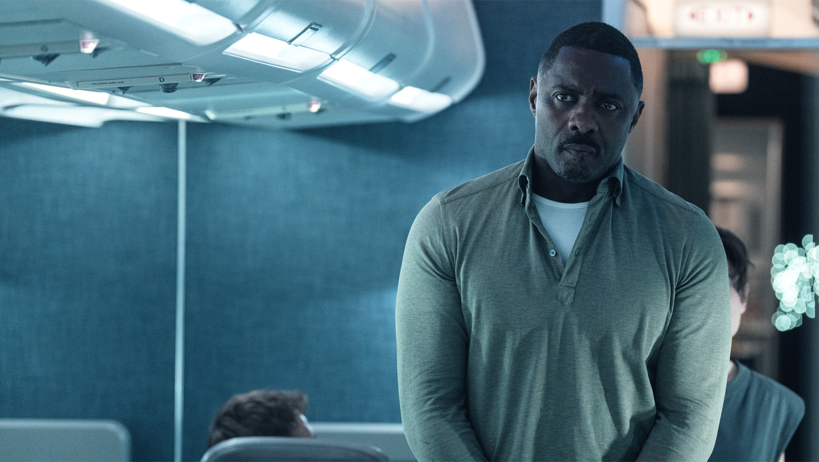 Idris Elba with his hands tied standing in an airplane in Apple TV Plus’ Hijack