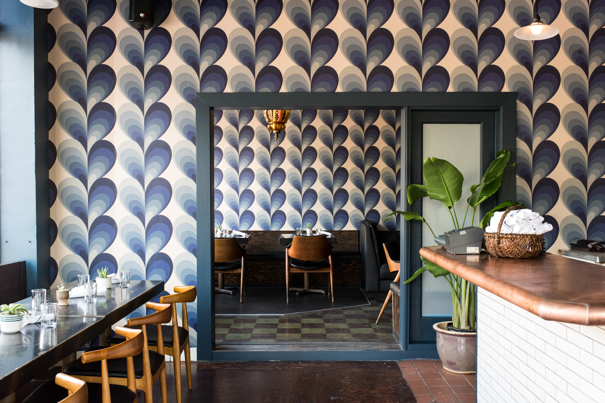 An empty restaurant dining room with blue-patterned wallpaper.
