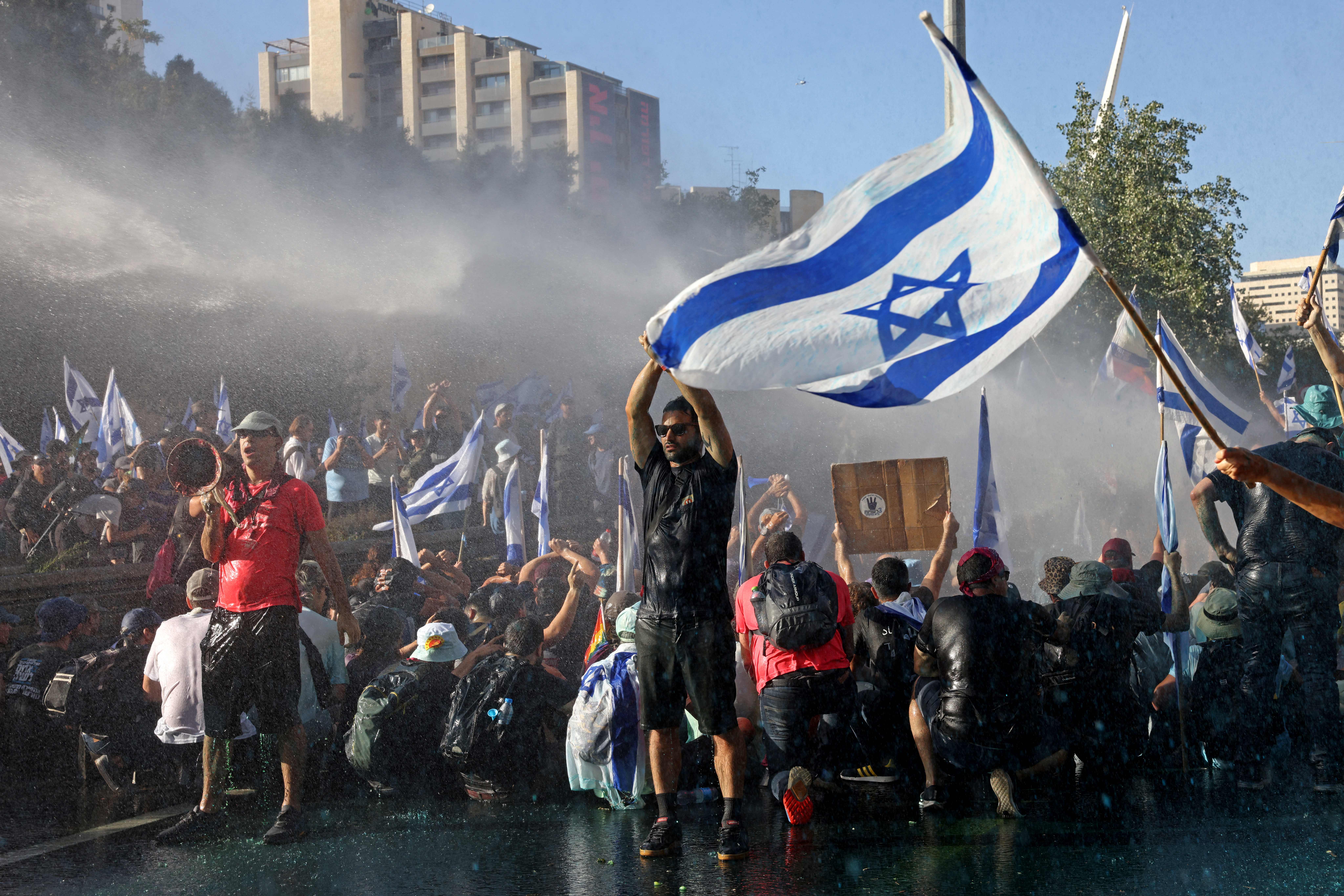 A mass of protesters, many holding Israel flags, are sprayed with water