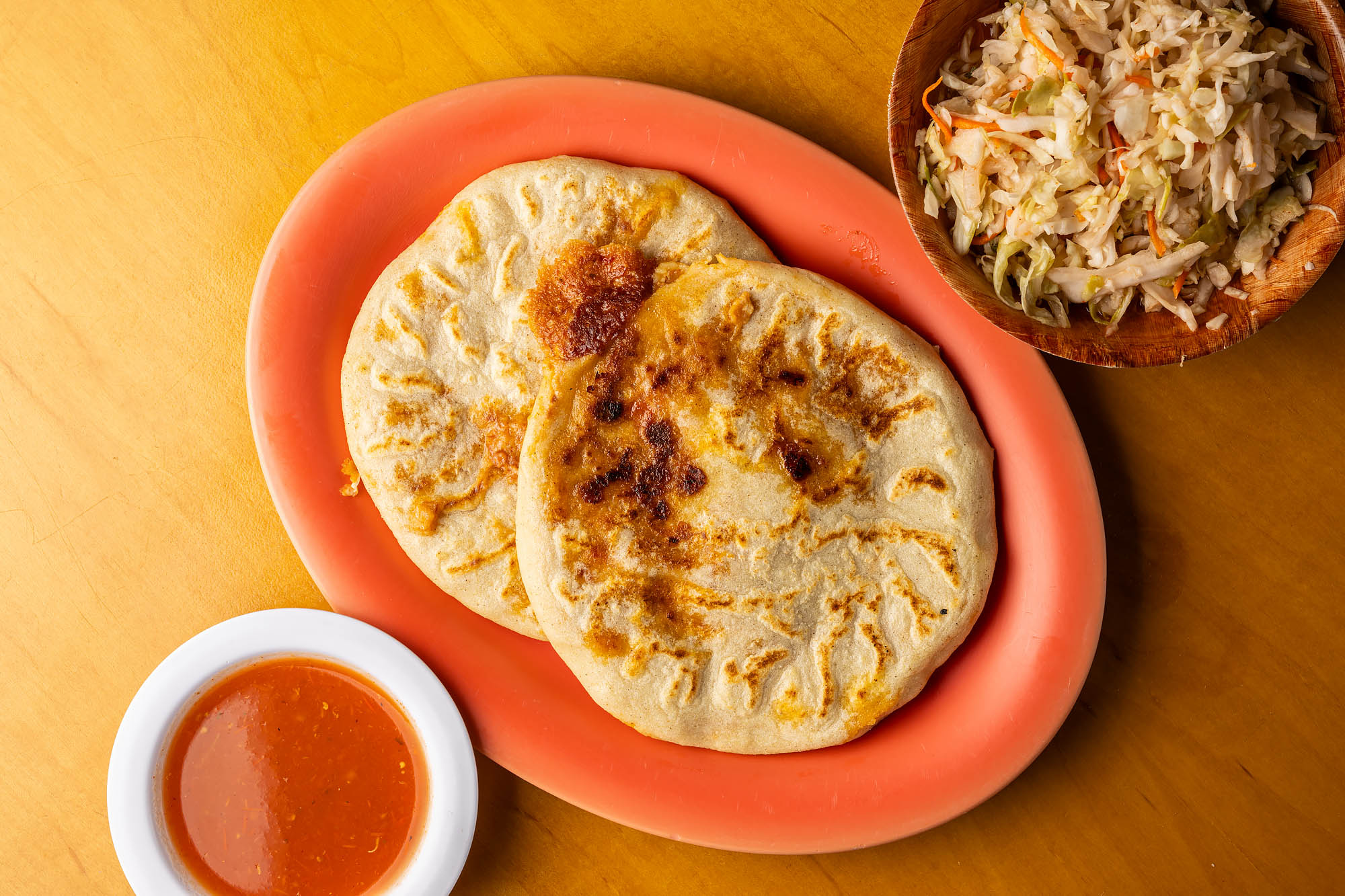 A plate of pupusas, plus salsa and curtido, on a table at Las Cazuelas.