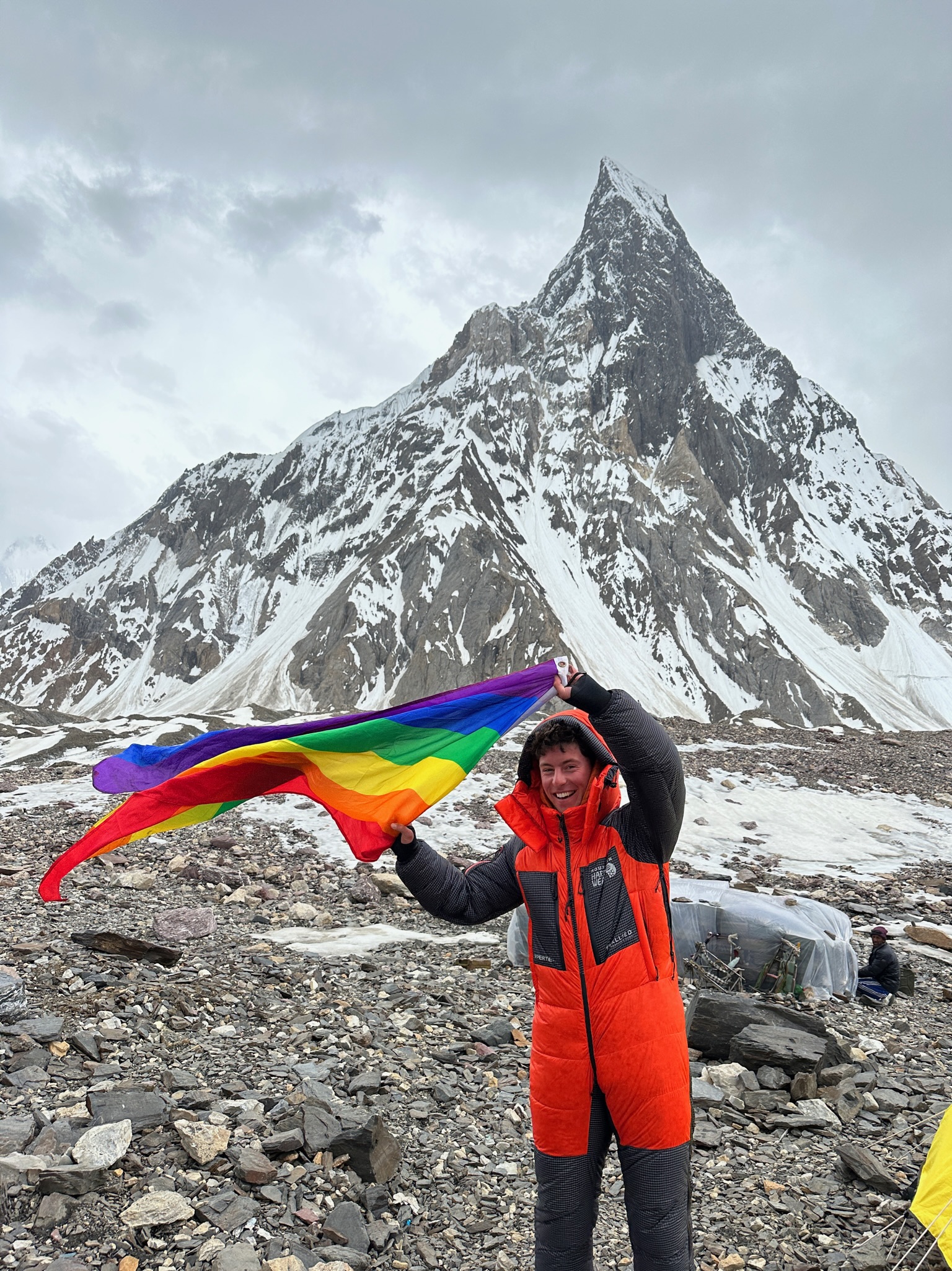 Queer mountain climber Aidan Hyman with rainbow flag on mountain.