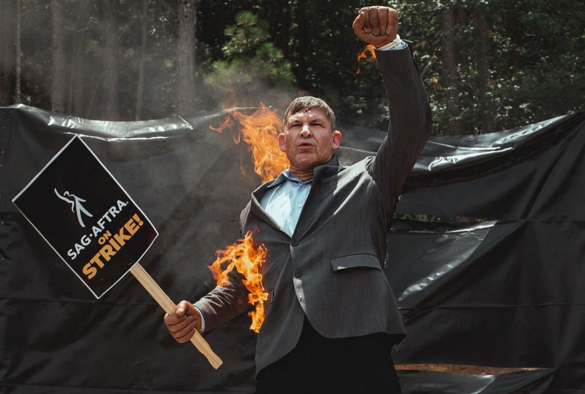 Stunt actor Mike Massa, wearing a suit and holding a strike sign, sets himself on fire at Atlanta picket line.
