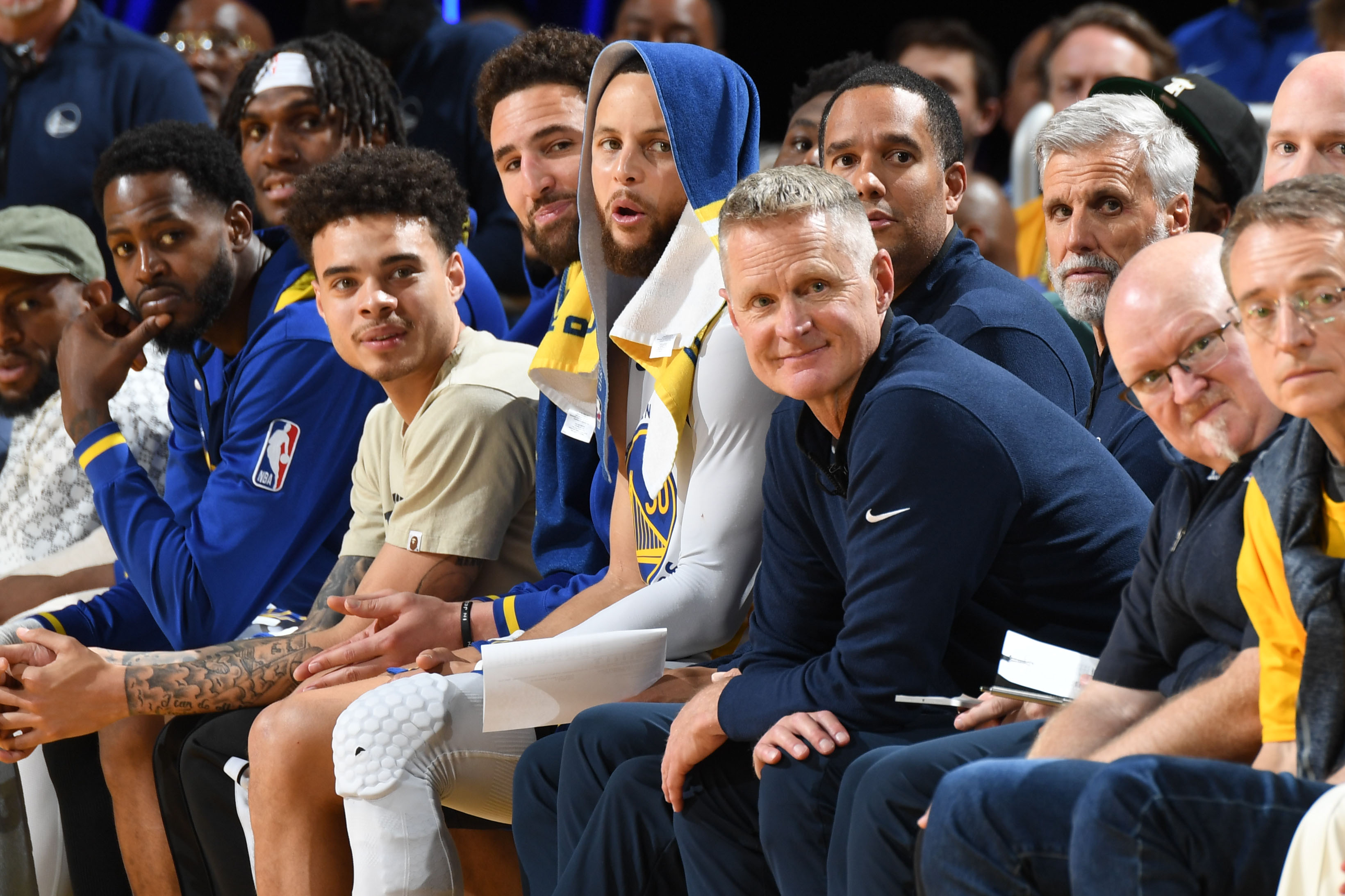 Steve Kerr and Steph Curry sitting next to each other on the bench