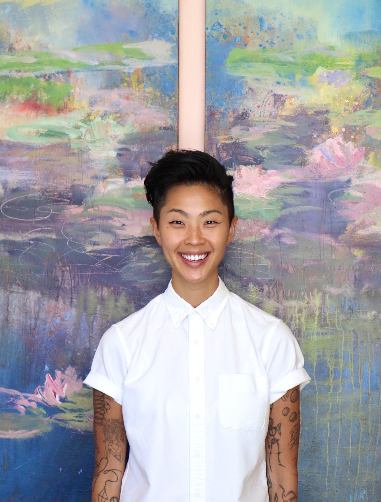 a headshot of celebrity chef and new Top Chef host Kristen Kish standing in front of a pastel colored painting