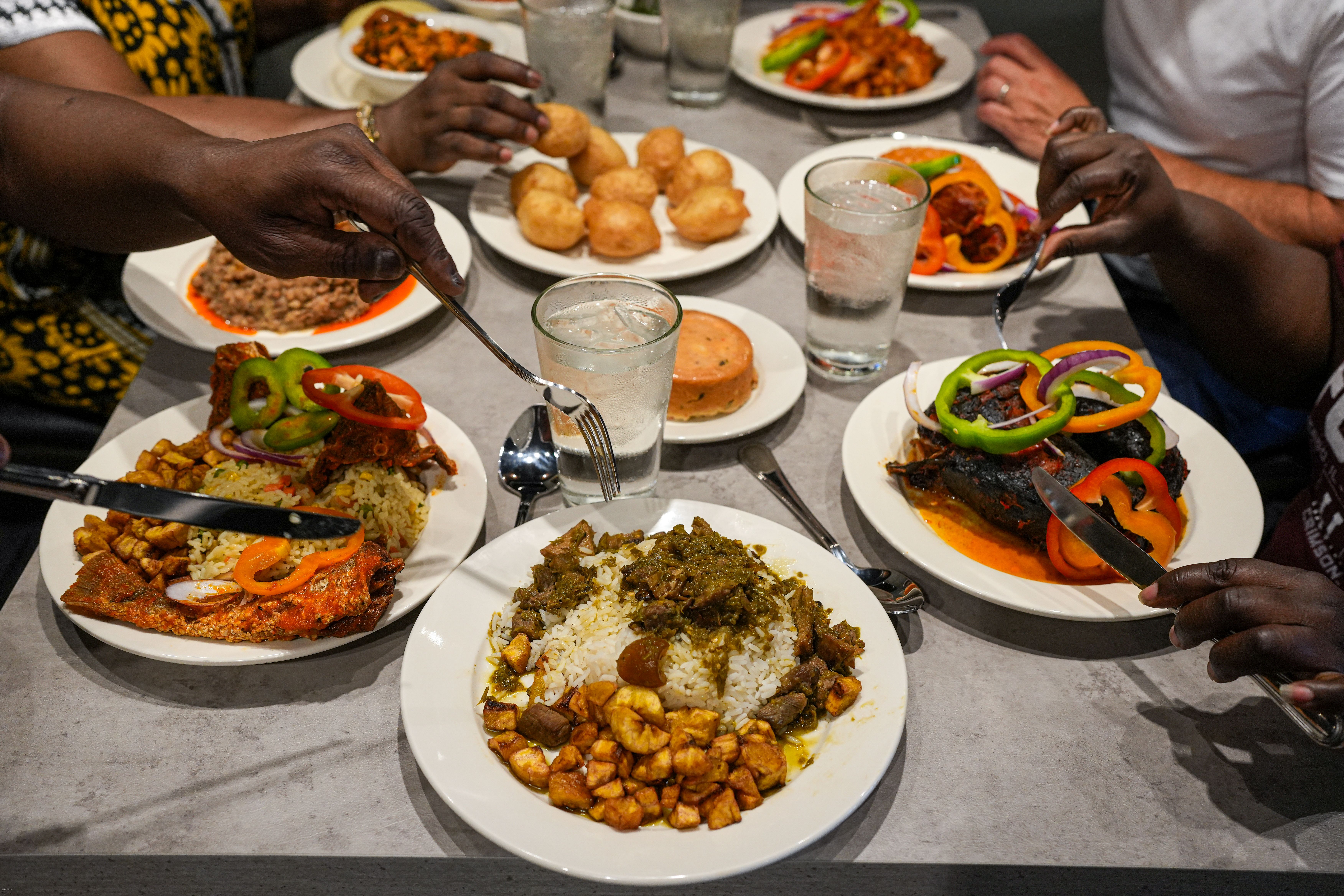 A dining room table with several diners eating African dishes that includes asun (grilled goat meat with spices), jolloff rice, and peppered snail.