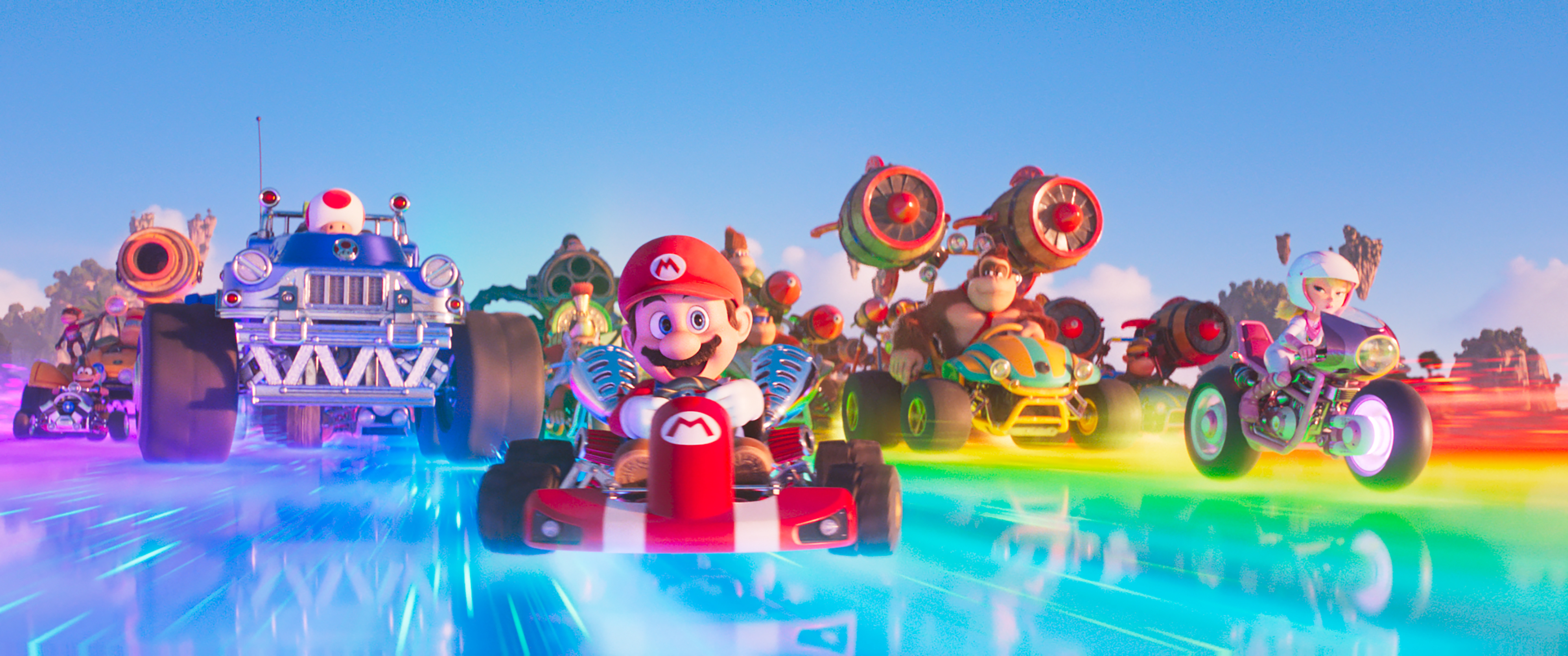 Mario and the cast of the Mario Bros. Movie in their Mario Kart vehicles as they speed down Rainbow Road.