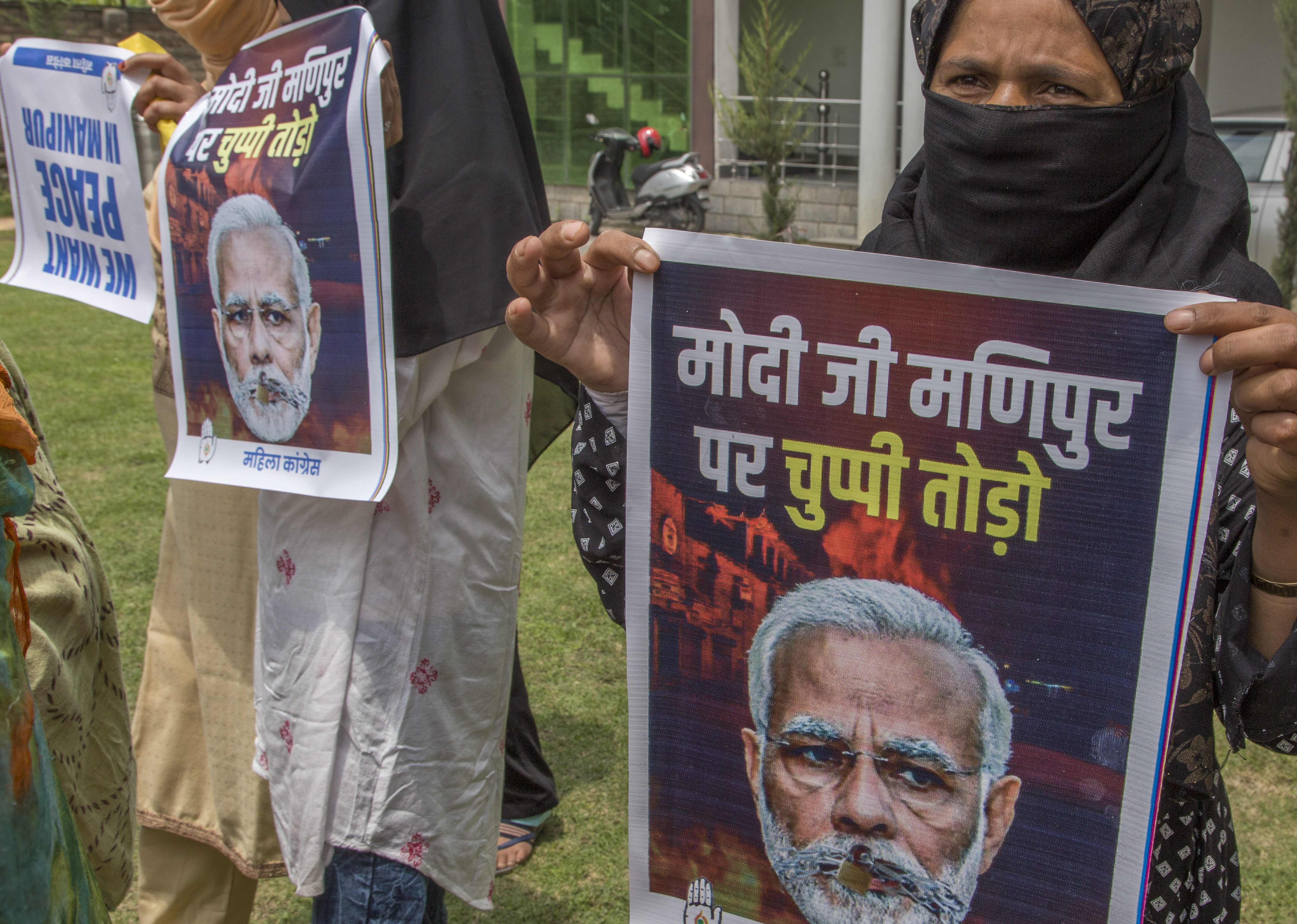 Women hold up protest posters with Narendra Modi’s face printed on them.