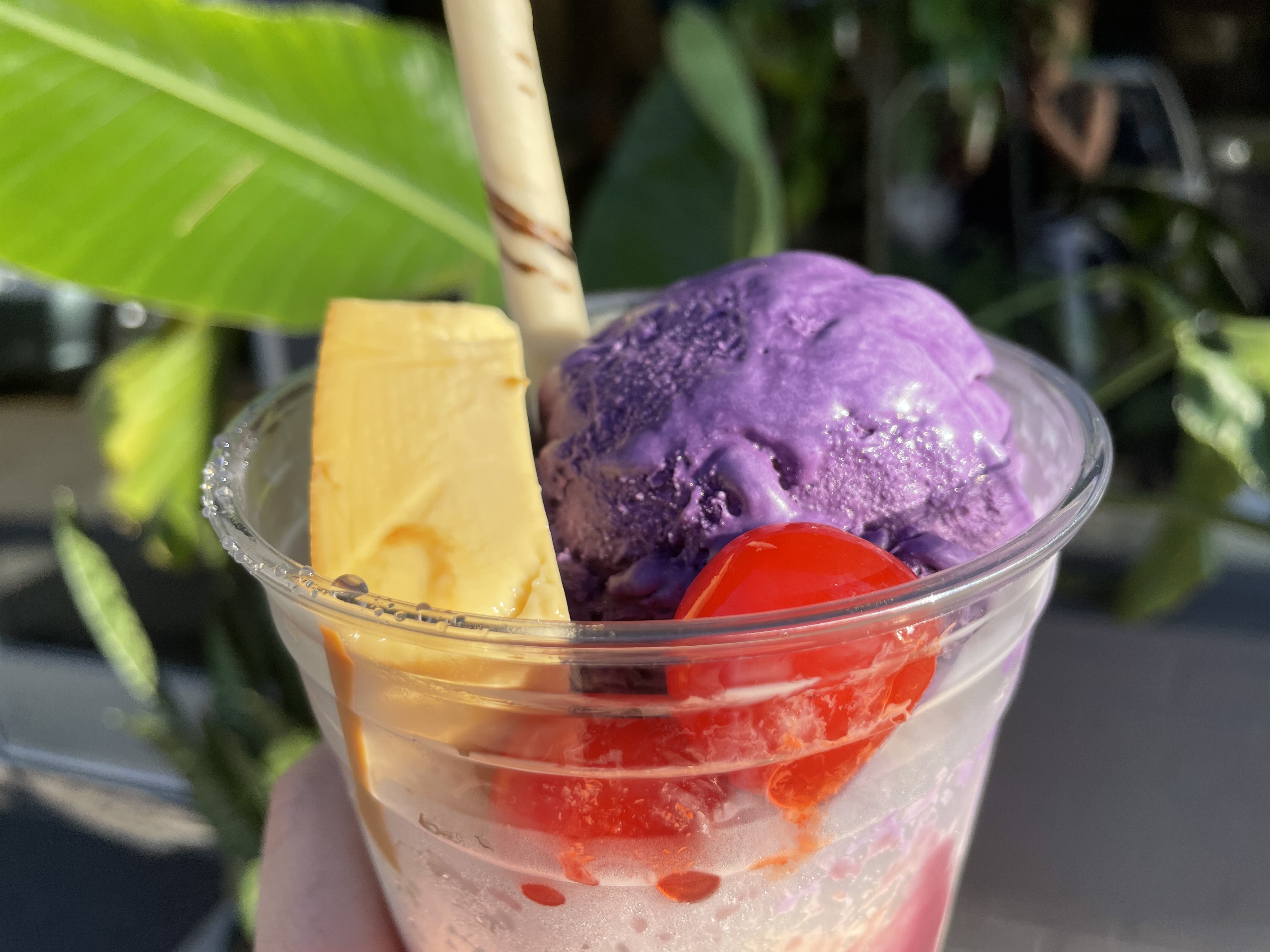 A cup with a scoop of purple ube ice cream, a square of lychee fan, and cherries above crushed ice, with a wafer sticking out of it.