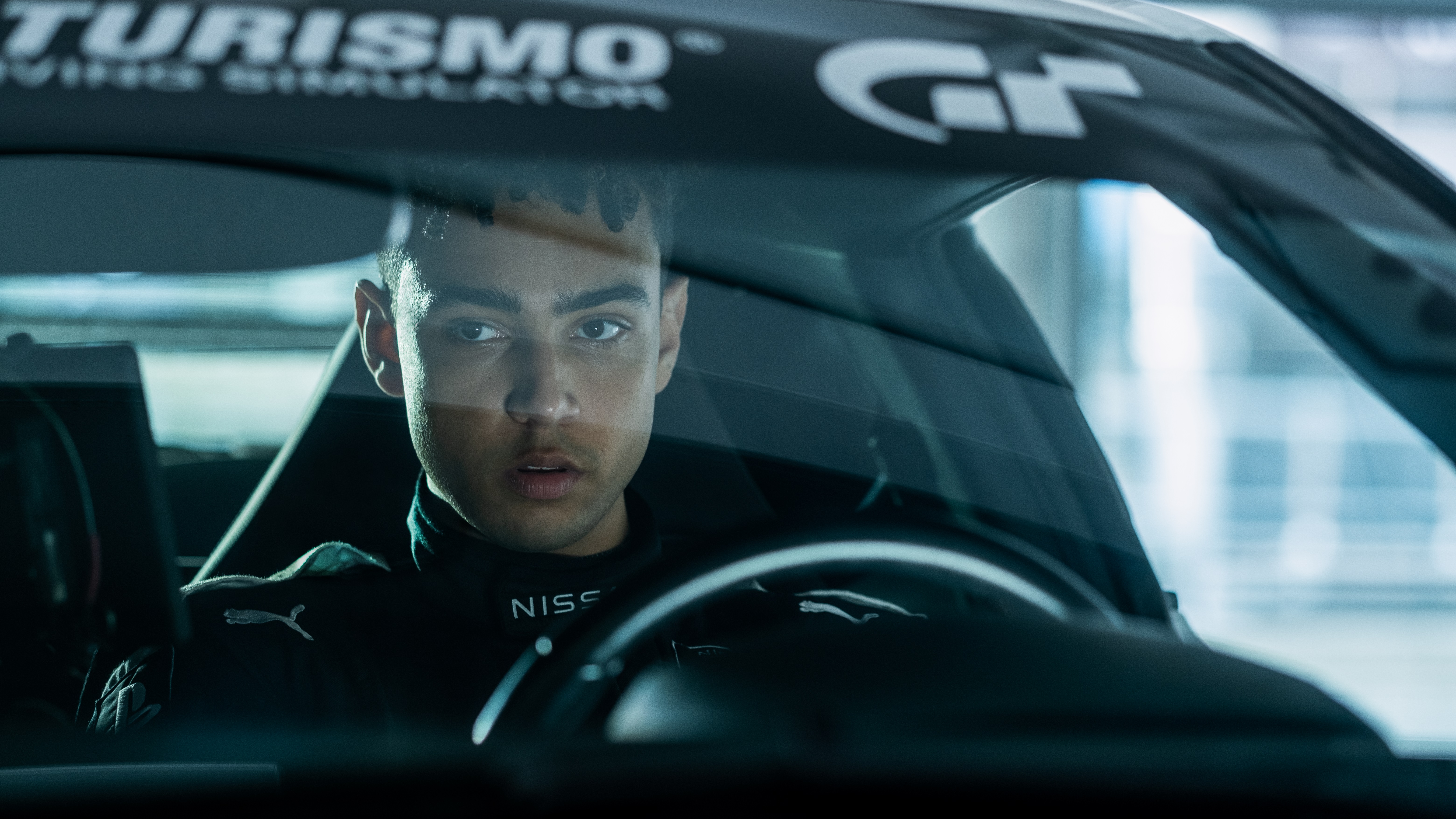 Archie Madekwe as Jann Mardenborough behind the wheel of a car with a Gran Turismo decal on the windscreen