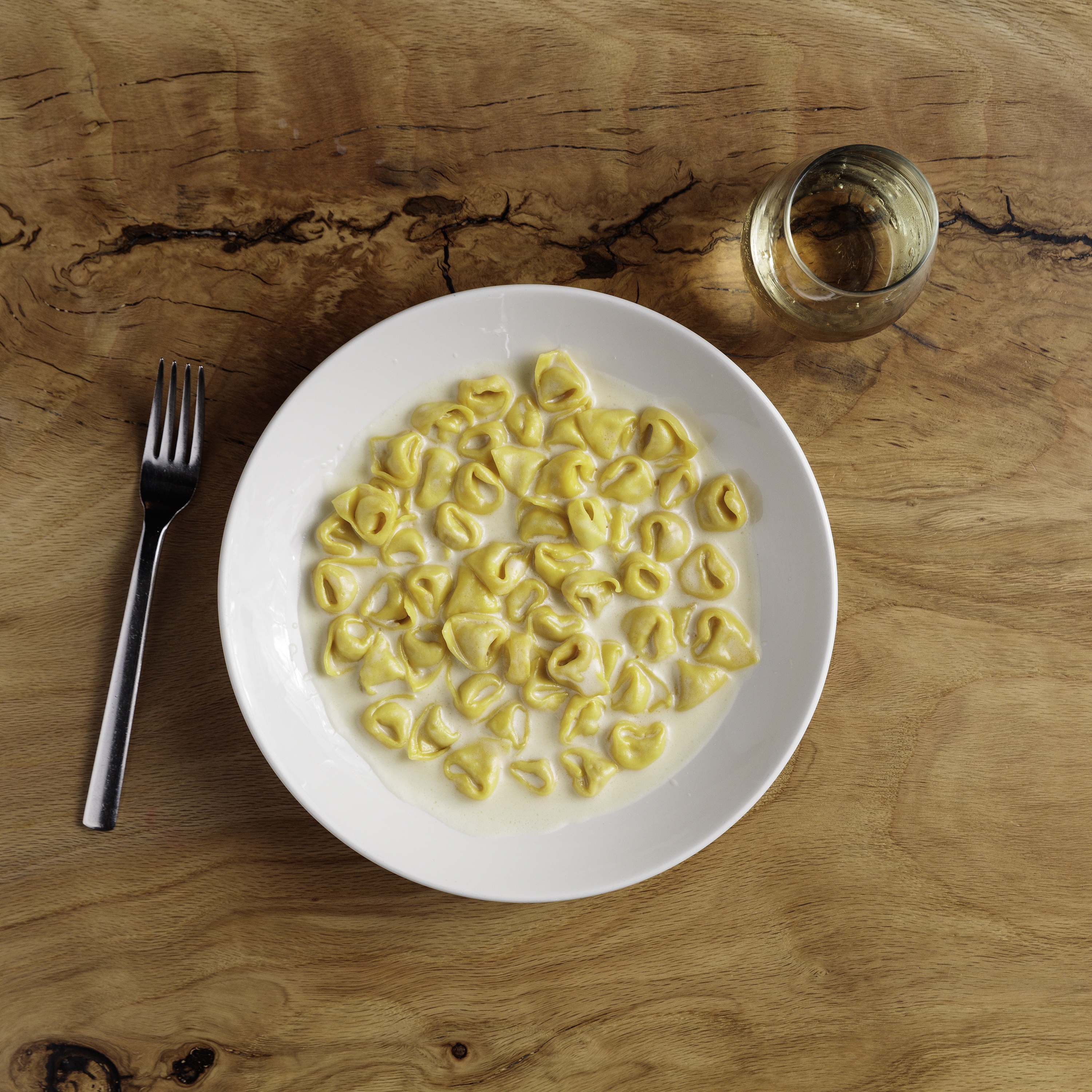 Bowl of tortellini in a white cream sauce on a wooden table.